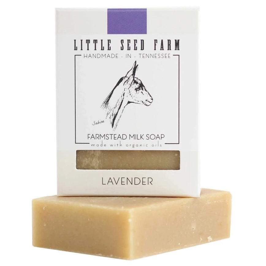A creamy bar of Little Seed Farm soap rests on a white surface with its packaging behind it. The box shows a goat and the words Lavender.