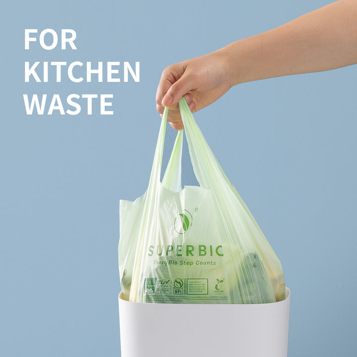 A hand pulls a light green "Superbio" bag filled with kitchen waste from a white bin. Large text in the top left corner of the image reads "FOR KITCHEN WASTE".