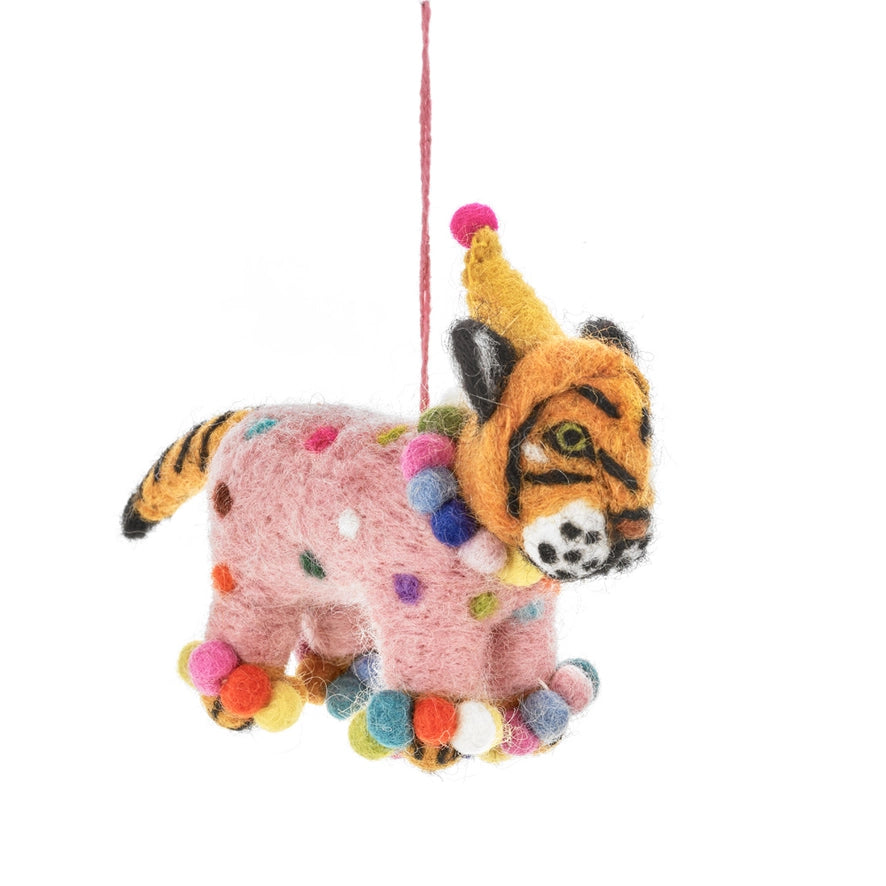 A handmade felt tiger cub is shown with a pink body covered in multicolored polka dots and multicolored pom-poms around its neck and feet. The tiger is also wearing a yellow party hat with a pink pom-pom on top.
