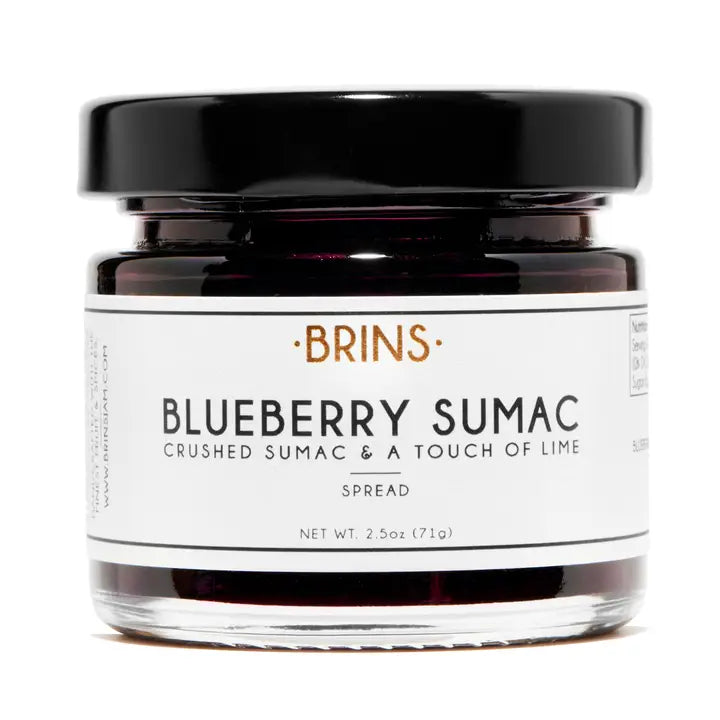 A small glass jar of "BRINS" Blueberry Sumac spread with a black lid. features the flavor and a description, "CRUSHED SUMAC & A TOUCH OF LIME" in black text. The rich dark purple spread is visible inside the jar.