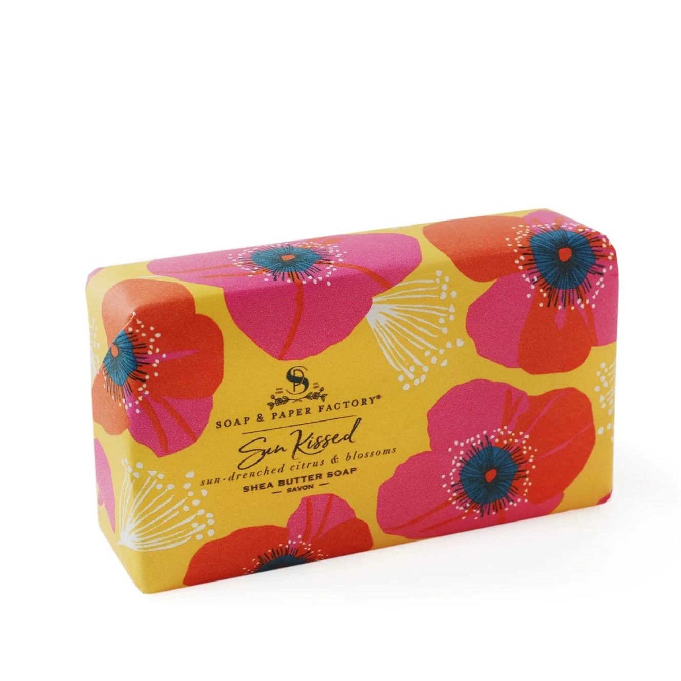 A vibrant yellow-wrapped 'Soap & Paper Factory' shea butter soap bar with a pattern of large pink flowers. The label for "Sun Kissed" also lists the scents "sun-drenched citrus & blossoms."