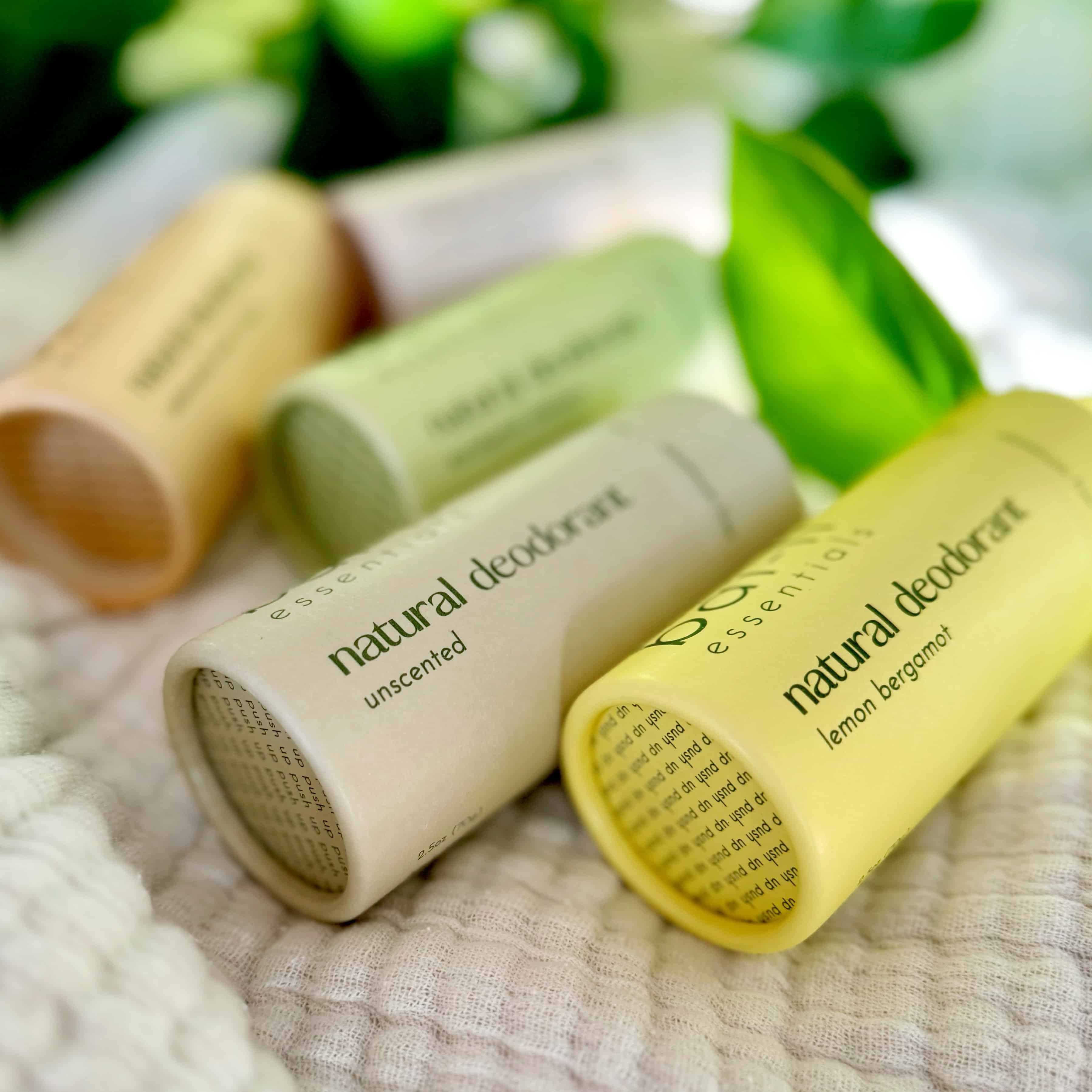 Close-up of four plastic-free deodorant tubes on a folded towel, showing Lemon + Bergamot, Unscented, Eucalyptus + Rosemary, and Cedarwood + Sweet Orange scents. Made with organic coconut oil, shea butter, arrowroot starch, and essential oils.