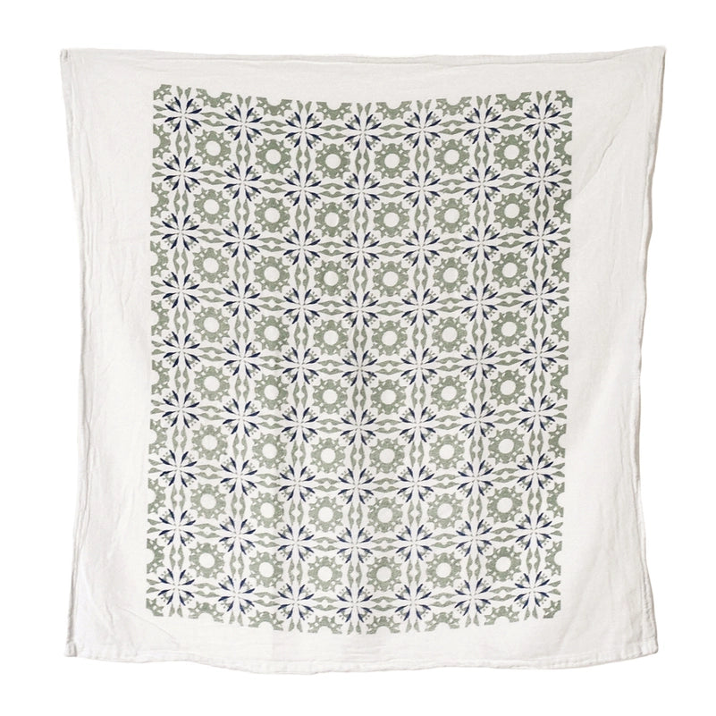 A white kithen towel features a charming, repeating geometric pattern in a mix of soft sage green, dark blue and white.