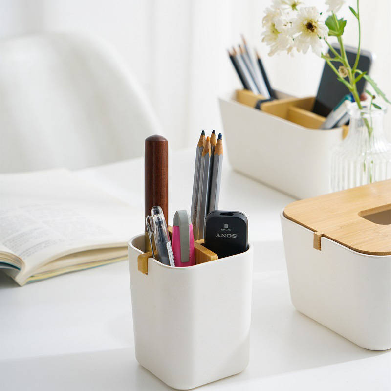 A small off-white caddy with a bamboo divider is holding a variety of writing tools including pencils a pen and a pink eraser.
