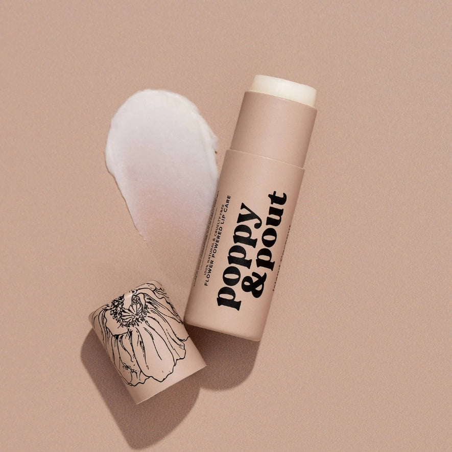An open tube of poppy & pout lip care is shown on a light tan background. The tube is labeled "FLOWER POWERED LIP CARE" and the cap has an illustration of a poppy flower. A creamy white product swatch is smeared next to the lip care tube.