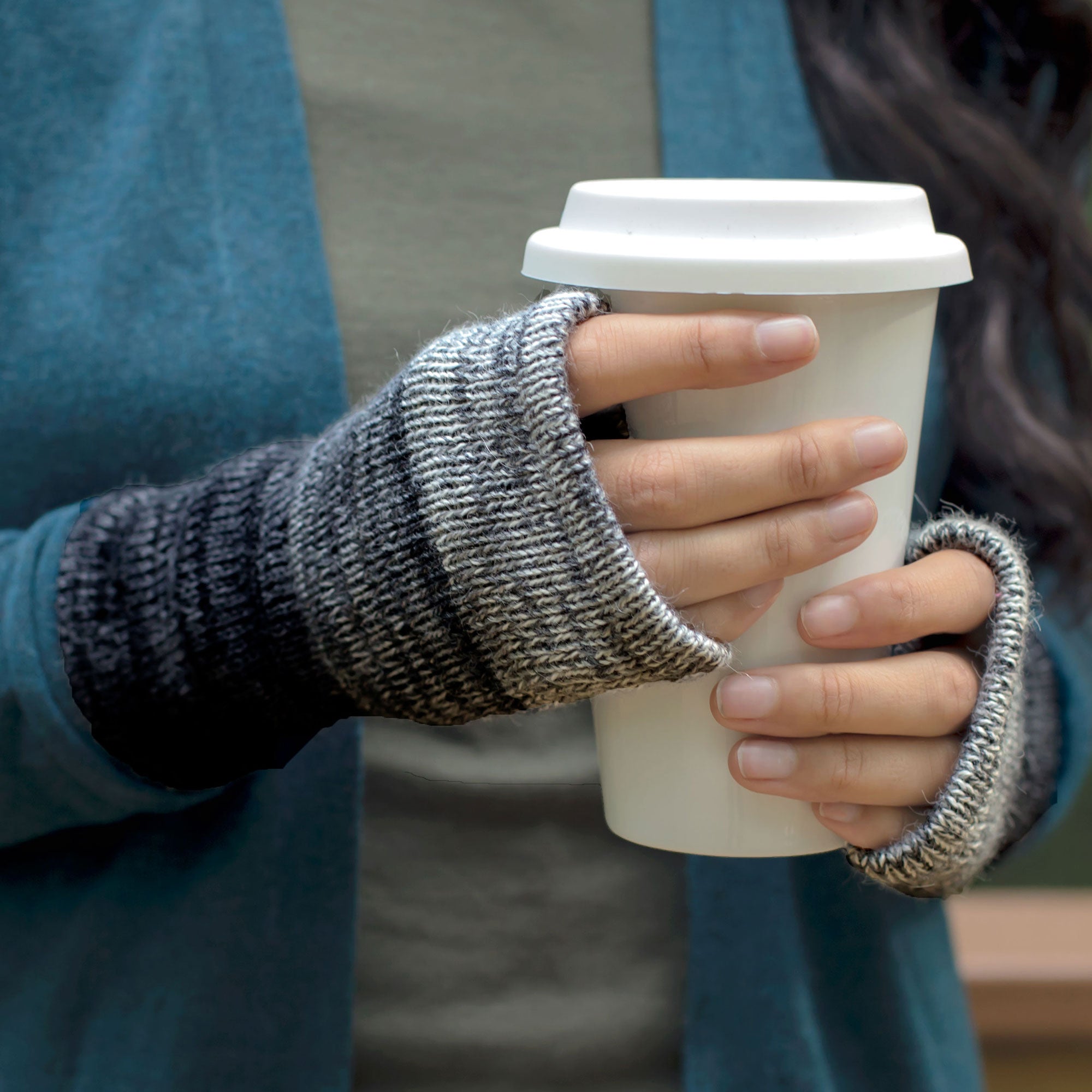 Two hands holding a paper cup while wearing gray and black handmade alpaca fingerless mittens.