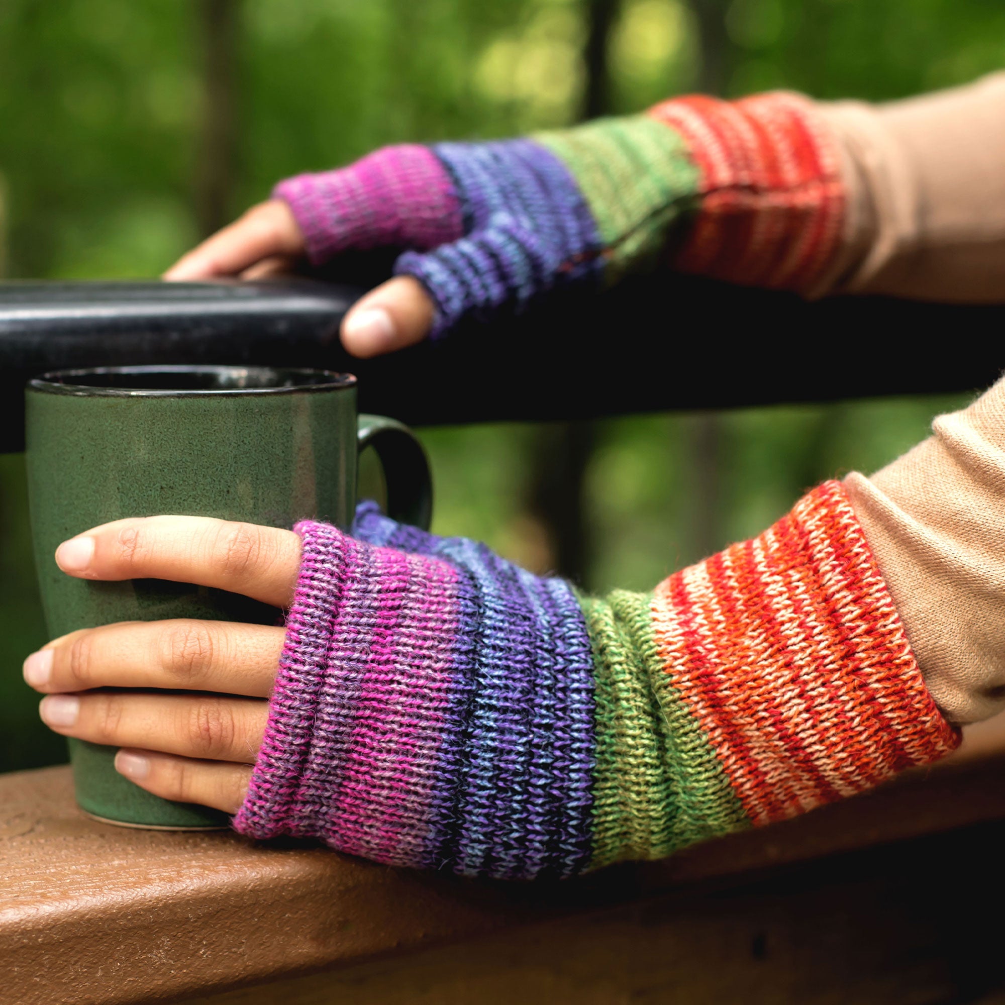 Close-up of hands wearing handmade alpaca fingerless mittens with a striped knit pattern in purple, blue, green, and red.