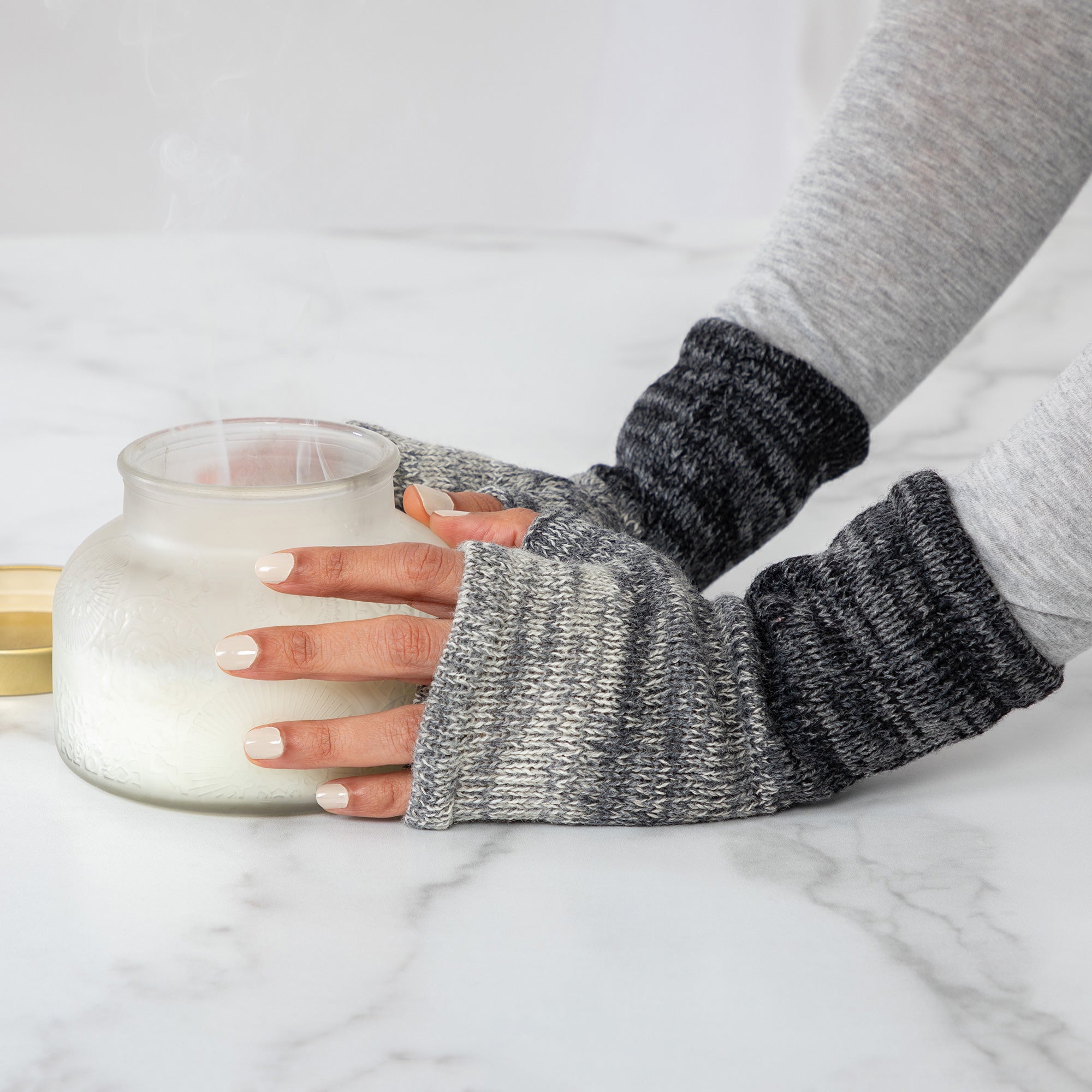 Hands holding a jar while wearing handmade black and gray alpaca fingerless mittens. Naturally soft and warm without bulk.