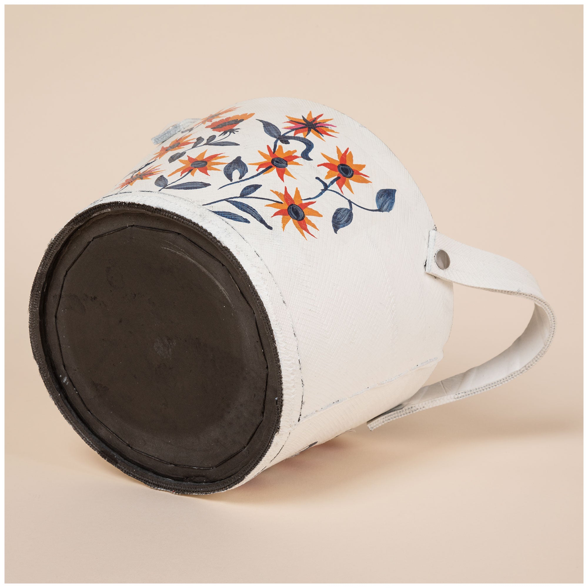 Small white planter made from recycled rubber, hand-painted with orange flowers and green leaves. Black interior visible with curved handles on both sides.
