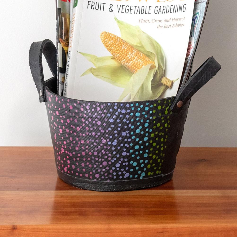A black storage bin with a colorful dotted pattern holds gardening books and seed packets, placed on a wooden surface.