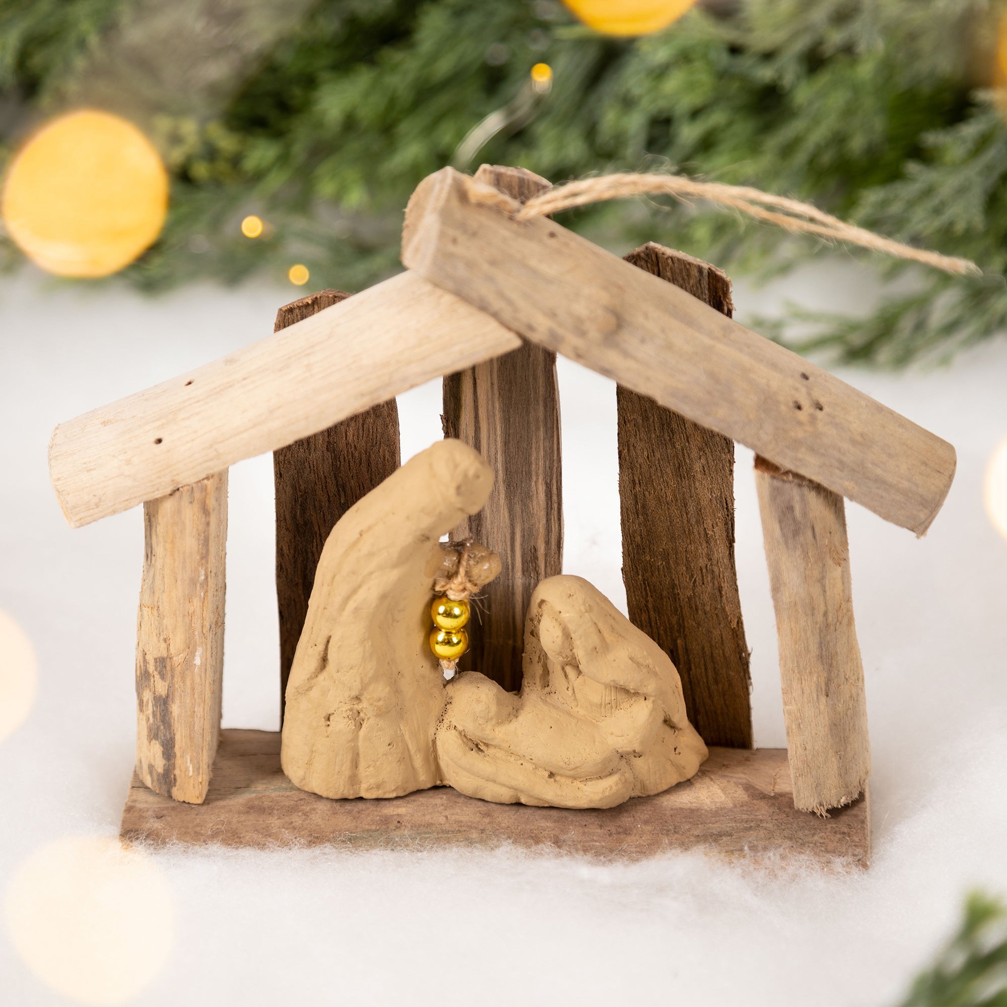 Handmade nativity ornament with recycled driftwood and clay figures, in front of a holiday tree, perfect for sustainable holiday decor.