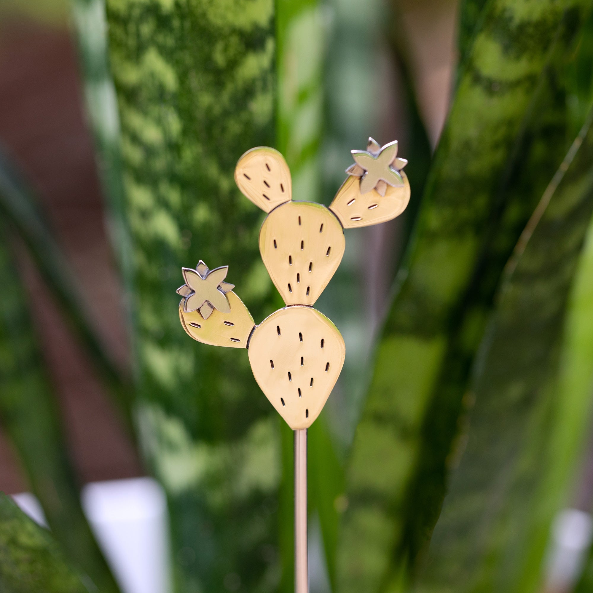 Close-up of a handmade cactus plant stake crafted from alpaca silver and brass, featuring etched details.
