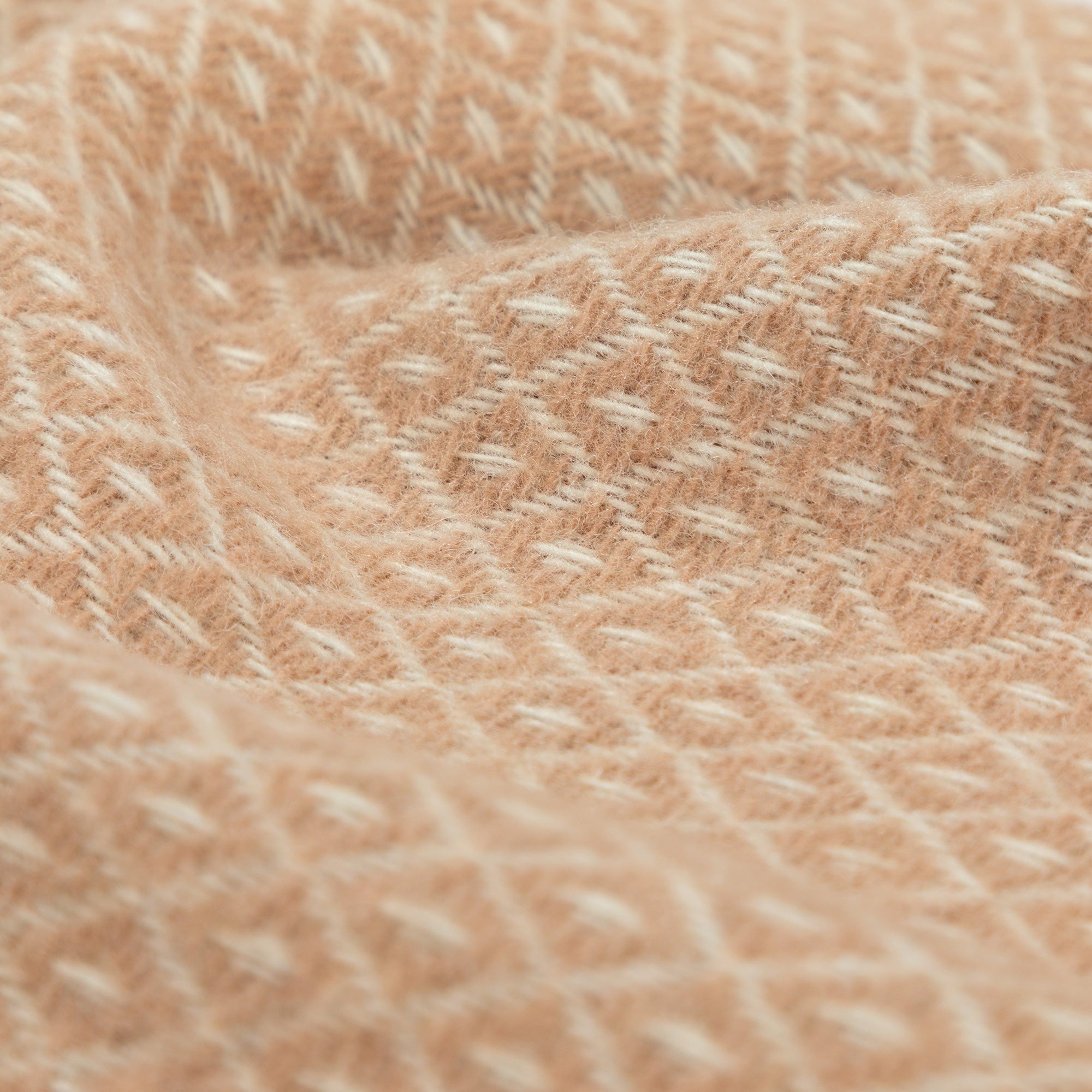 Close-up of a soft peach-colored 100% wool throw blanket, highlighting its textured diamond weave and handcrafted quality.