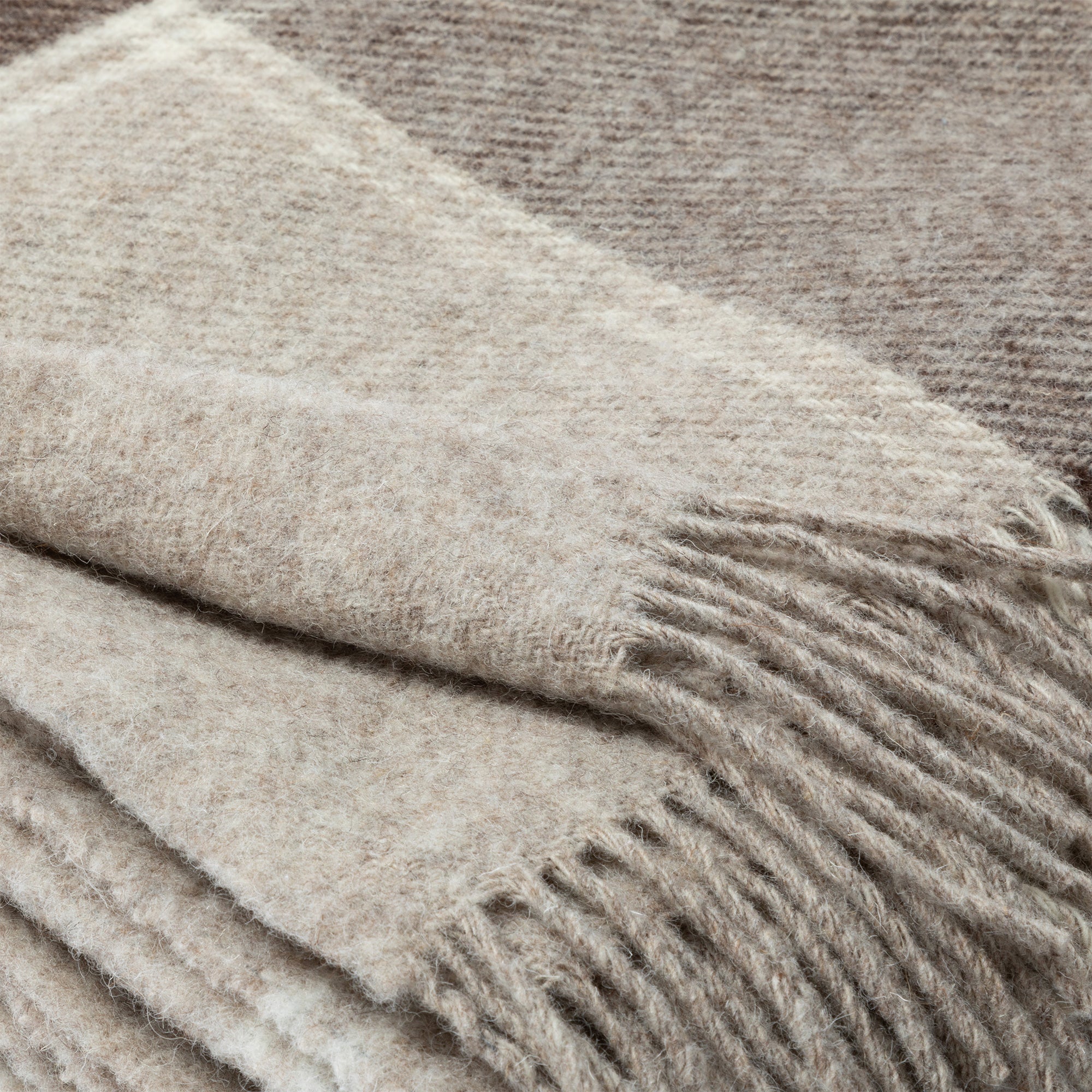 Close-up of soft, folded 100% wool throw blanket in neutral tones with fringe detail. Handcrafted in Ukraine.