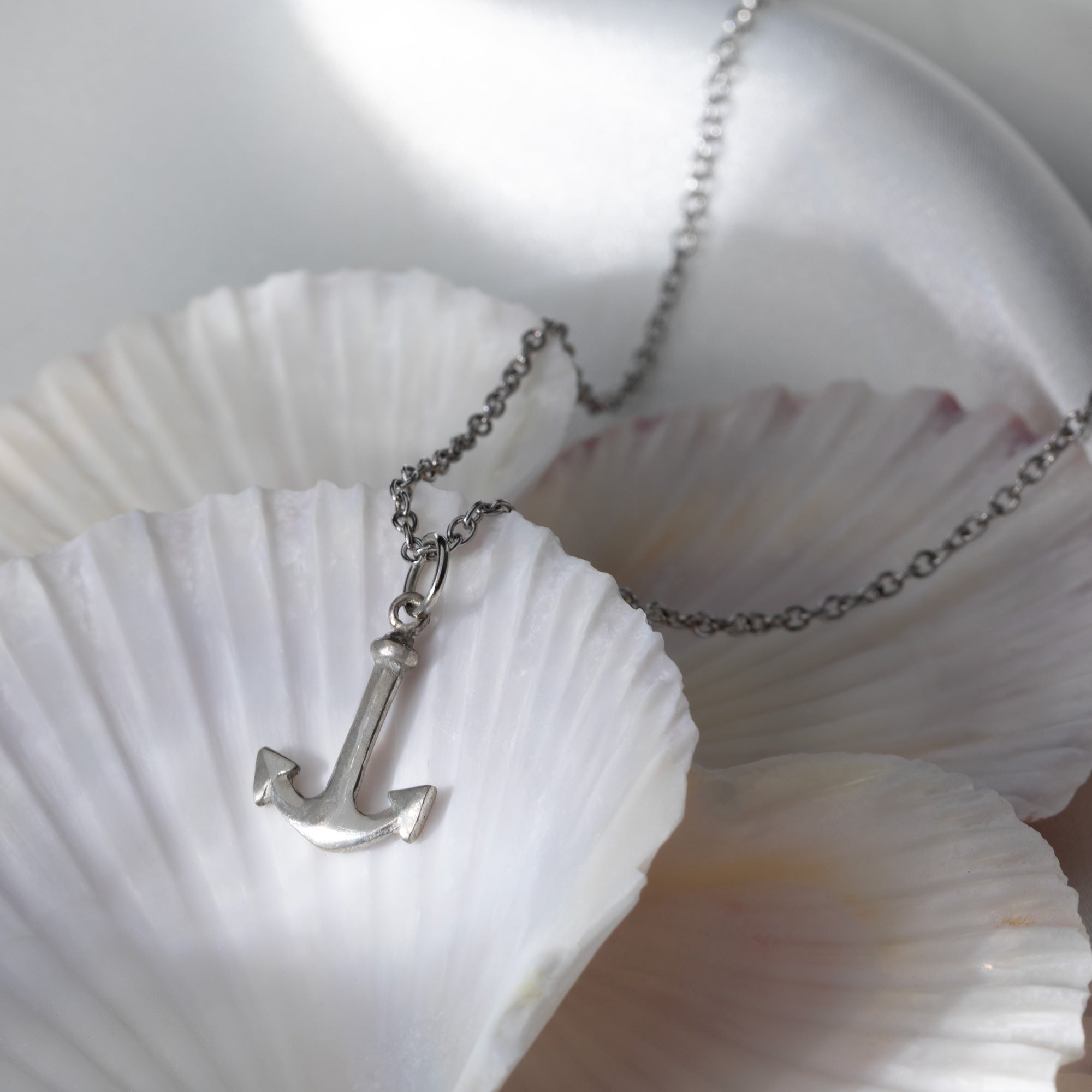 A pewter anchor necklace on a chain resting on a white seashell, designed to remind wearers of their connection to the ocean and the importance of conservation.