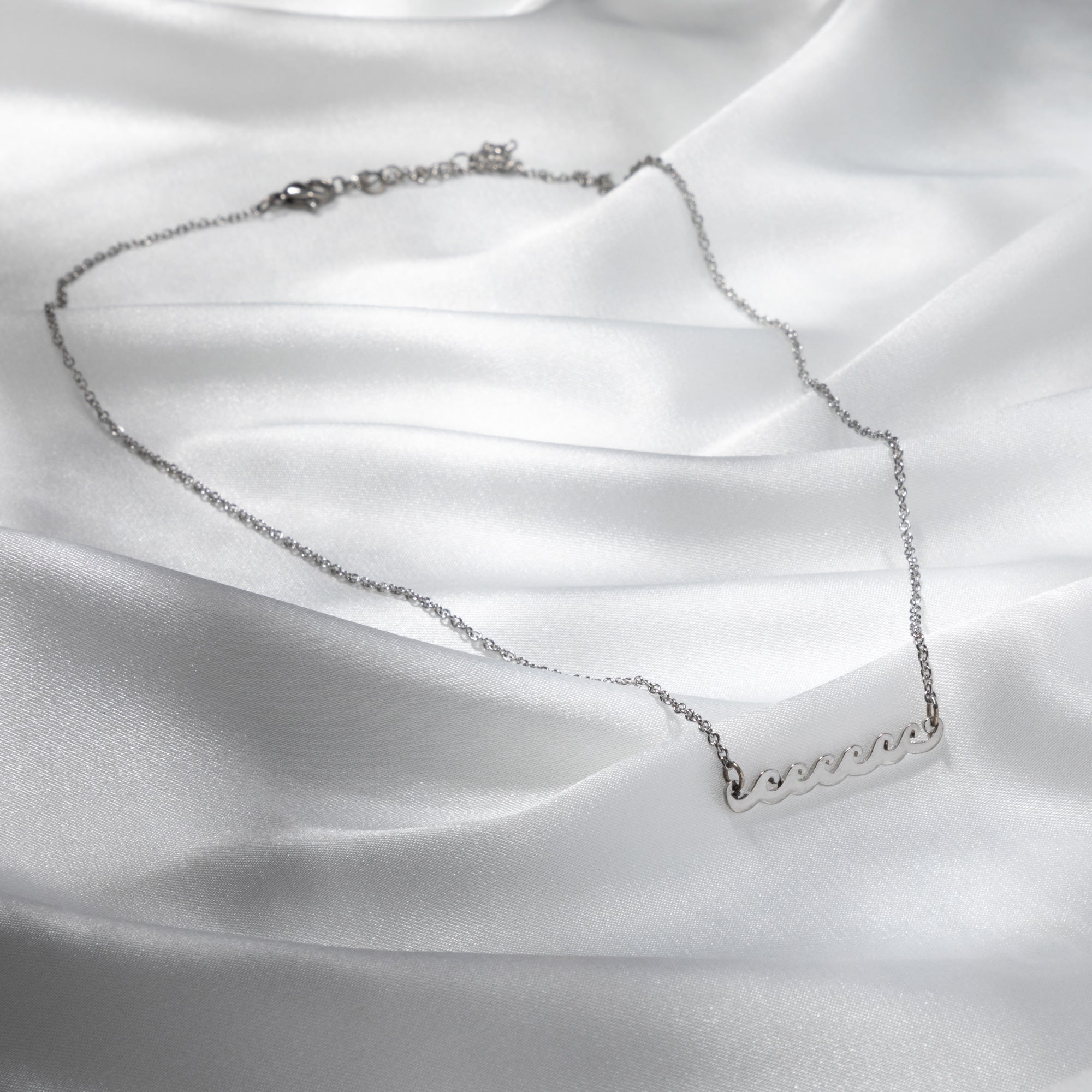 A pewter waves necklace lying flat on a white fabric background, symbolizing the beauty of the sea and crafted to support sustainable fashion initiatives.