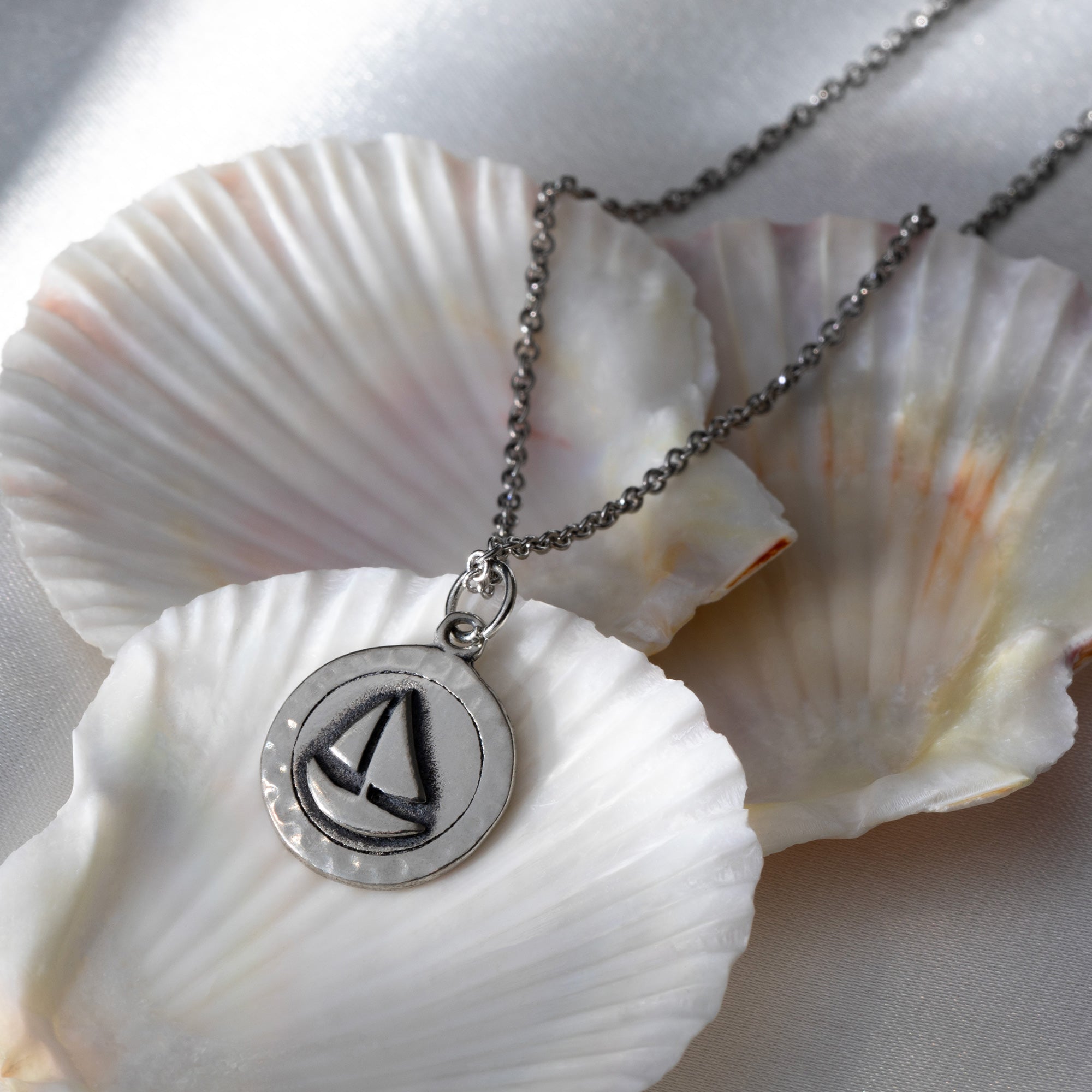 A delicate pewter necklace with a sailboat pendant on a chain, displayed indoors against a neutral background, reflecting nautical charm and sustainable craftsmanship.