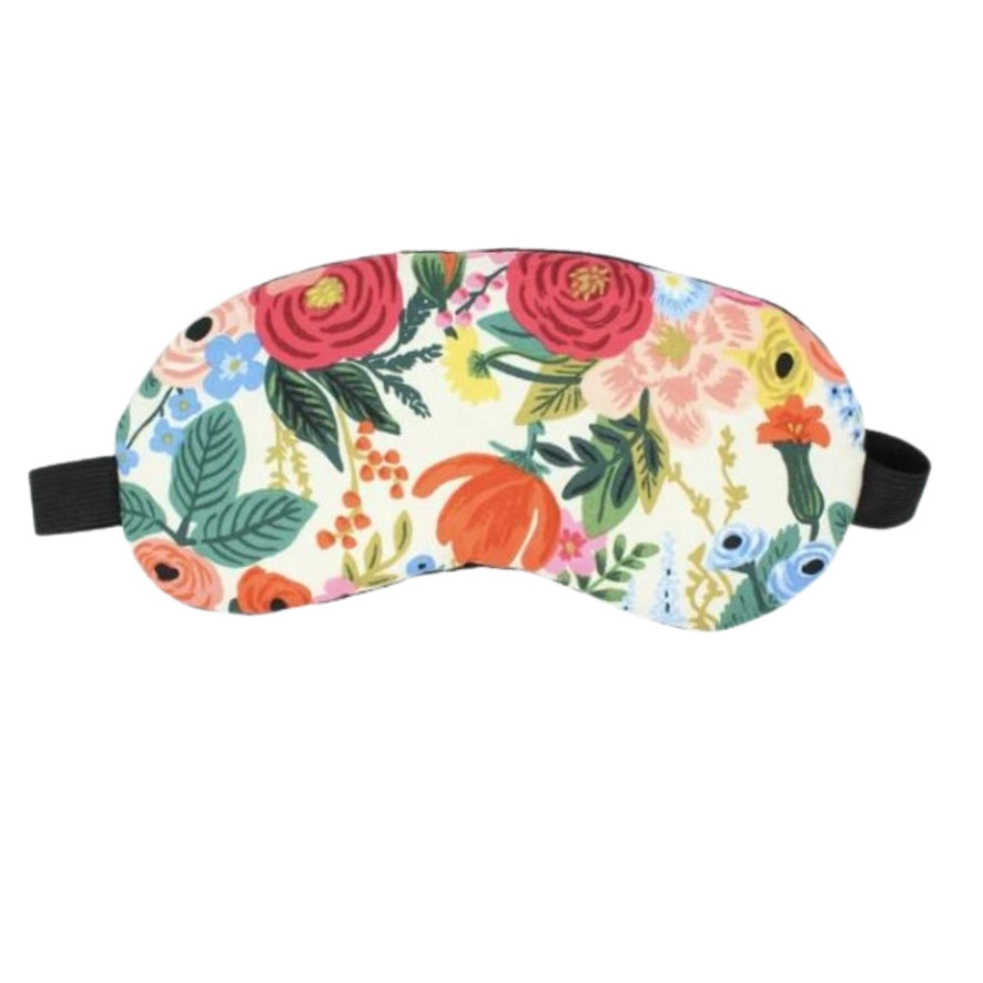 A handmade cotton eye mask with a floral pattern is shown against a white background. The mask has a pattern of red, pink, blue, yellow and green flowers, leaves, sporting a black elastic band.