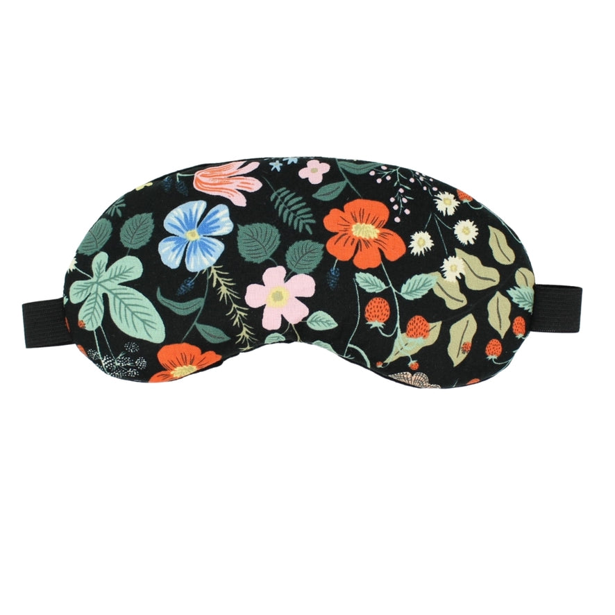 A black cottn eye mask with a vibrant floral pattern is shown against a white background. The mask is decorated with flowers in shades of pink, orange and blue, along with green leaves and small red berries. It has a black elastic band on the side.