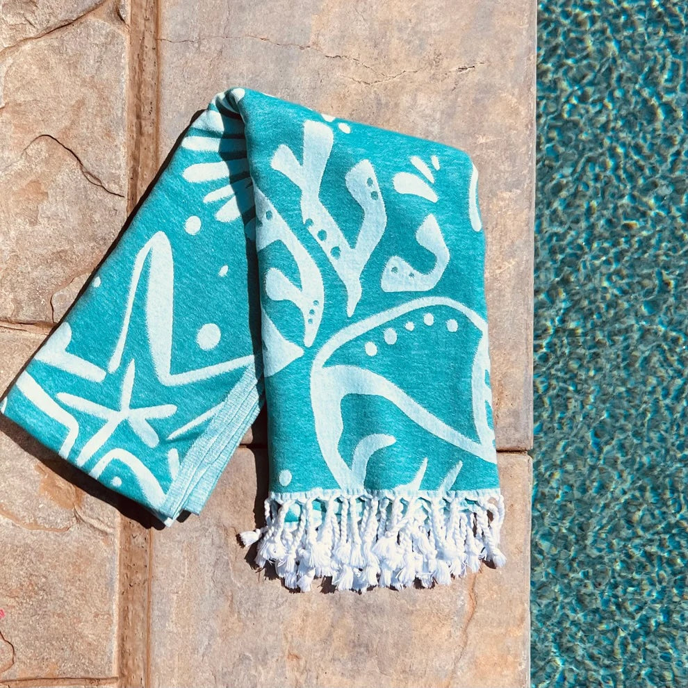 Teal and turquoise patterned Turkish towel resting on the edge of a swimming pool, made from upcycled cotton.