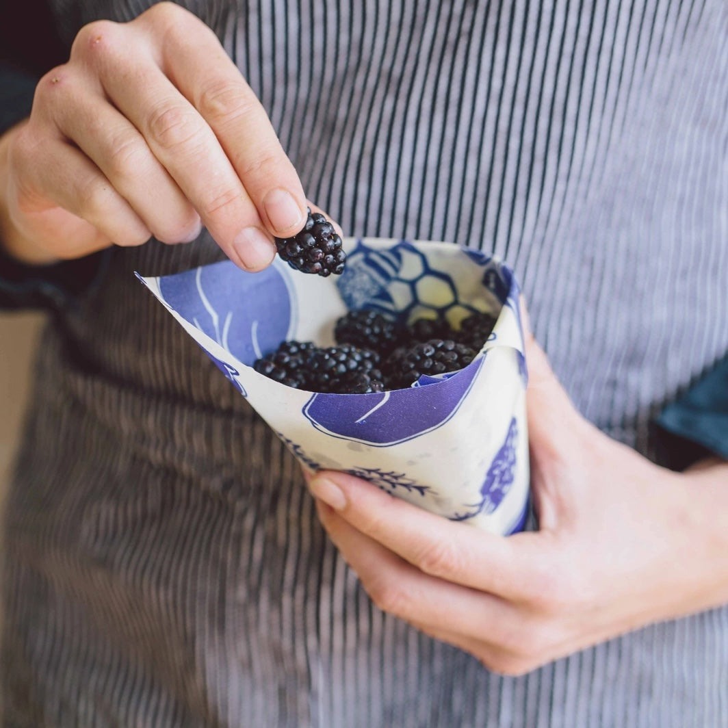 Hands holding a cone-shaped Bees Wrap with blue bear and bee pattern, filled with fresh blackberries.
