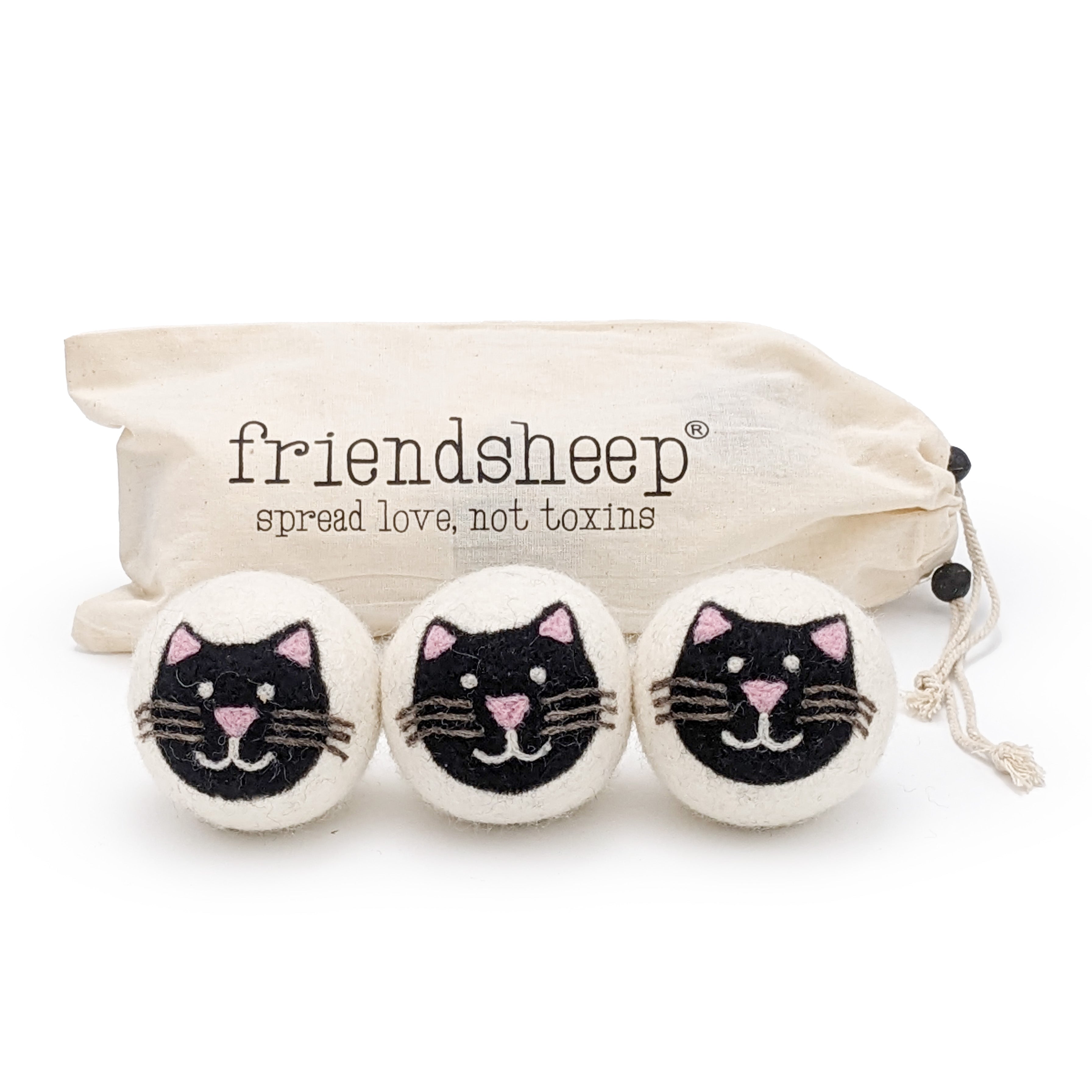 A set of three Friendsheep sustainable goods wool dryer balls are shown, each decorated with a cute black cat face. They are sitting in front of their white canvas drawstring bag.