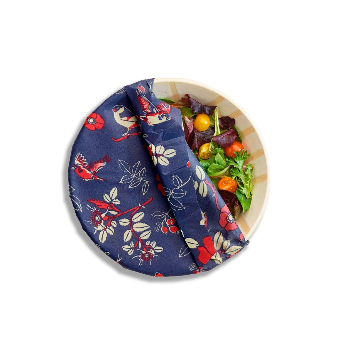Top-down view of a white bowl with mixed salad greens covered partially by a navy Bee’s Wrap with birds and floral print.