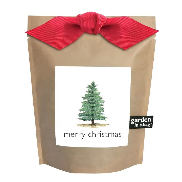 A festive brown paper "garden in a bag" pouch is tied with a red bow and features a label with a watercolor illustration of an evergreen tree and the words "merry christmas".