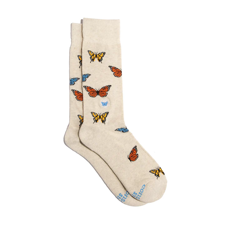 A pair of light-colored Conscious Step socks with a multi-colored butterfly pattern is shown against a white background.