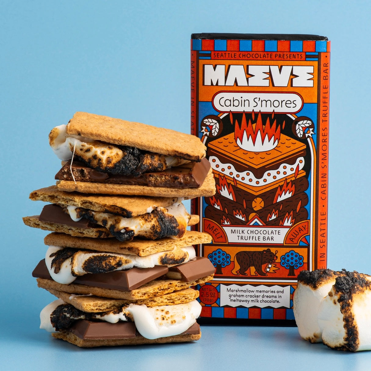 A stack of cookies layered with marshmallow and chocolate sits beside the Maeve "Cabin S’mores" truffle bar, evoking cozy campfire treats and highlighting the indulgent, ethically made flavor.