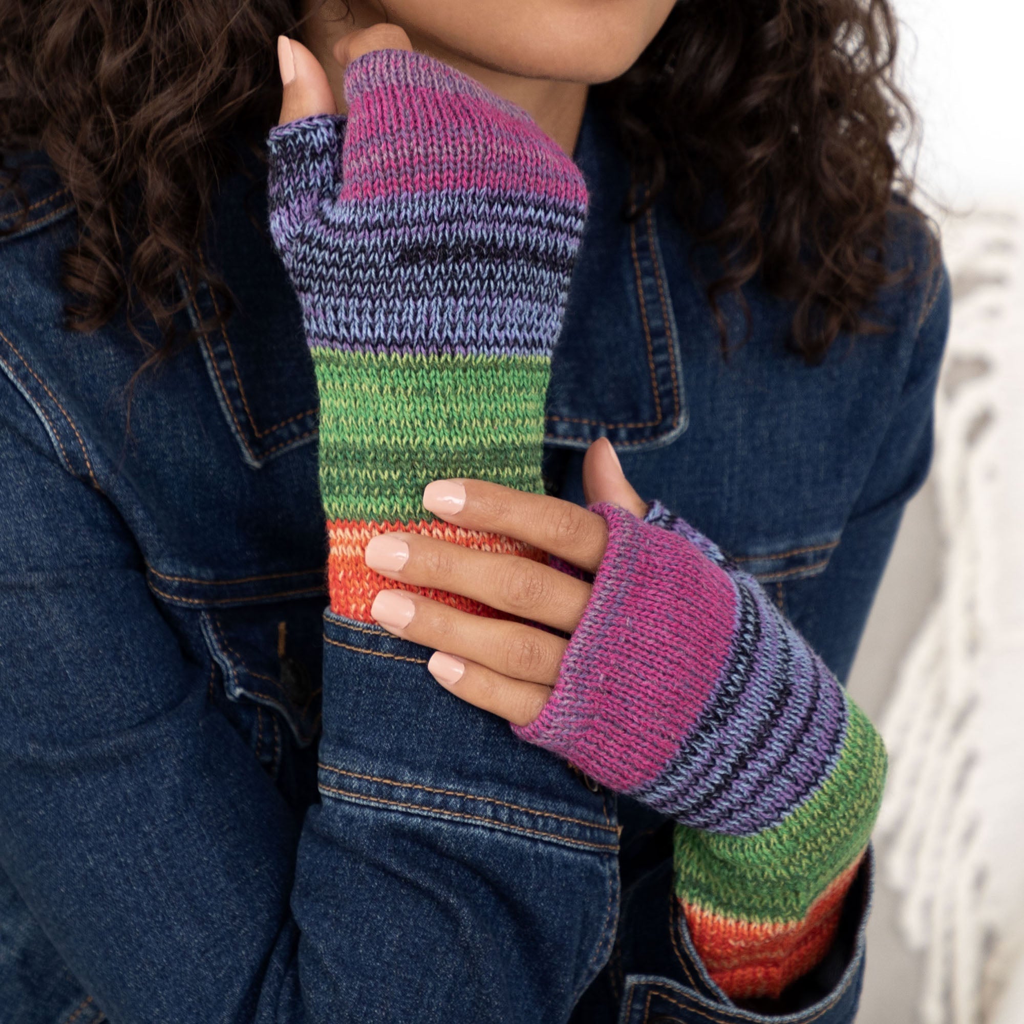 Woman wearing handmade alpaca fingerless mittens with colorful stripes in purple, blue, green, and red. Naturally warm and lightweight.