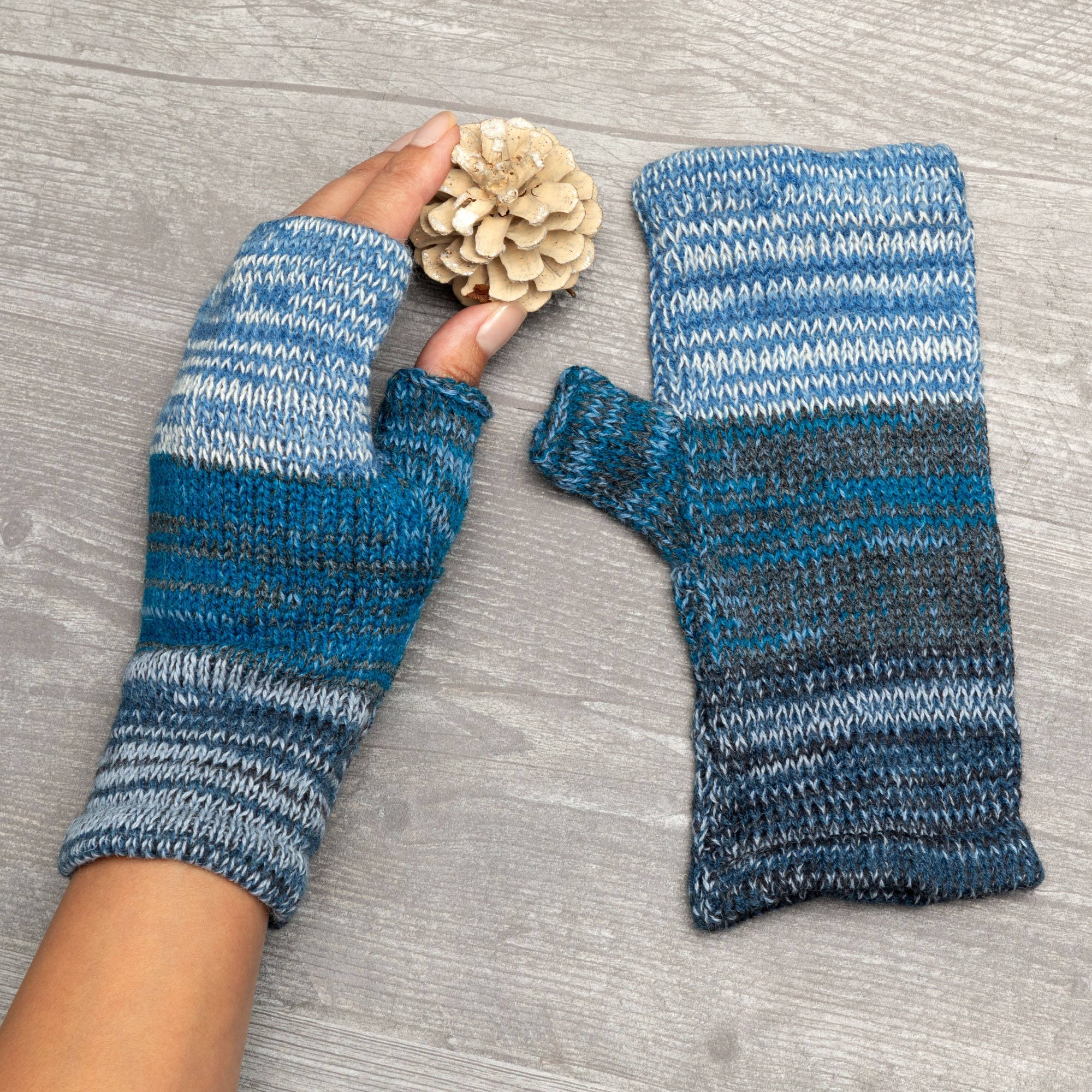 A pair of gloved hands wearing handmade alpaca fingerless mittens, with colorful threads and textured fibers visible.