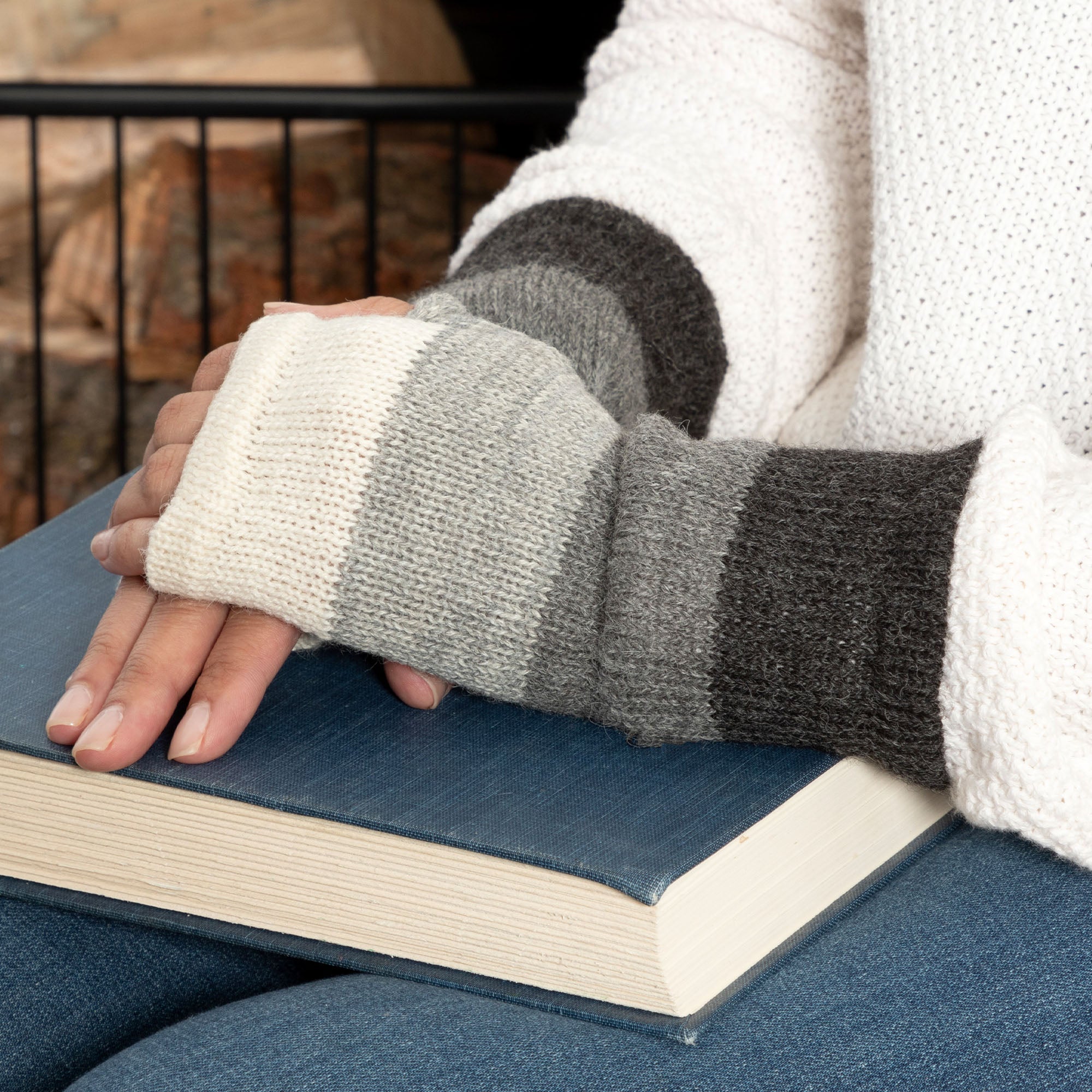 Person wearing white and gray striped handmade alpaca fingerless mittens.