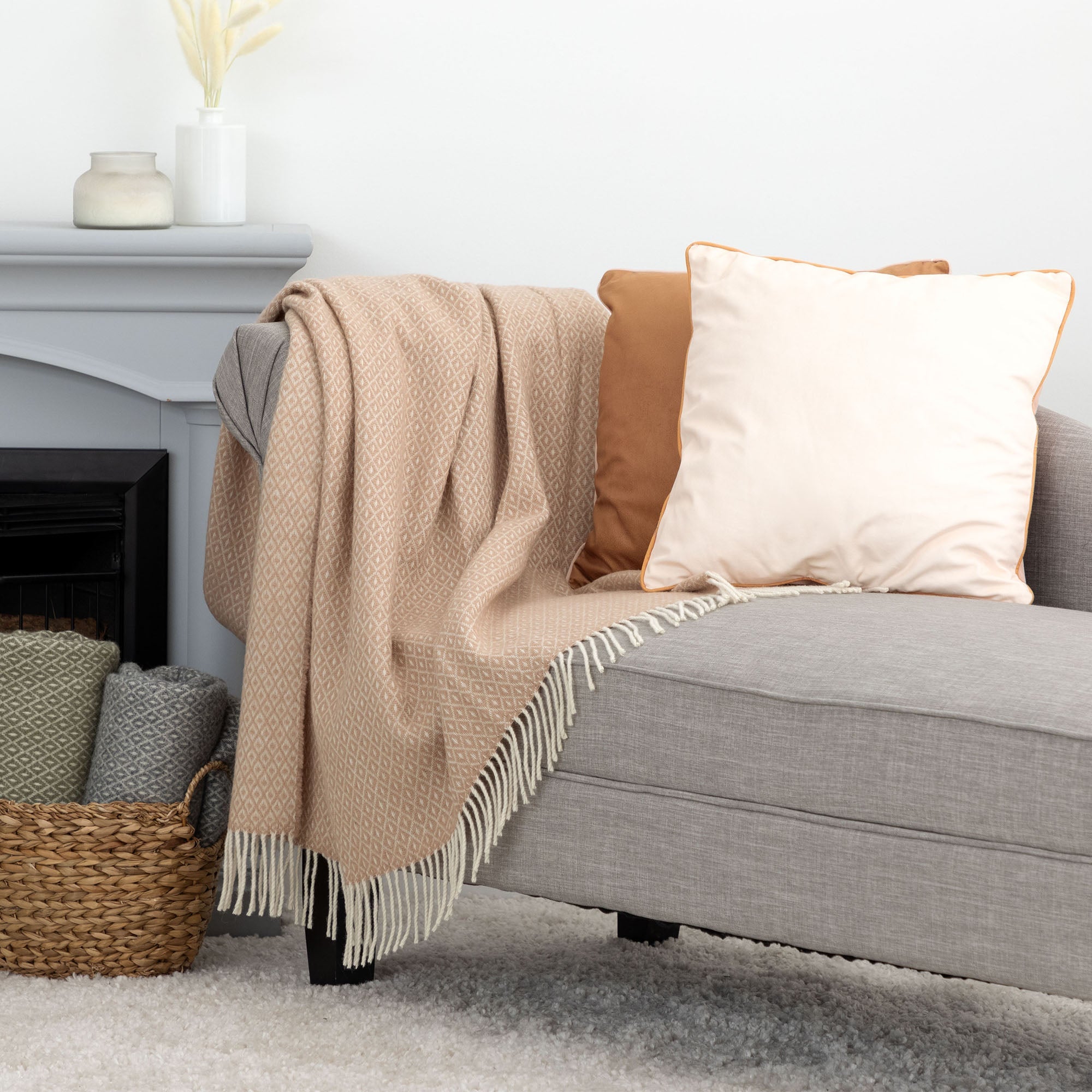 A cozy living room scene showing a light peach Ukrainian blanket draped over a gray upholstered armchair next to a woven basket filled with folded blankets in green and gray tones.