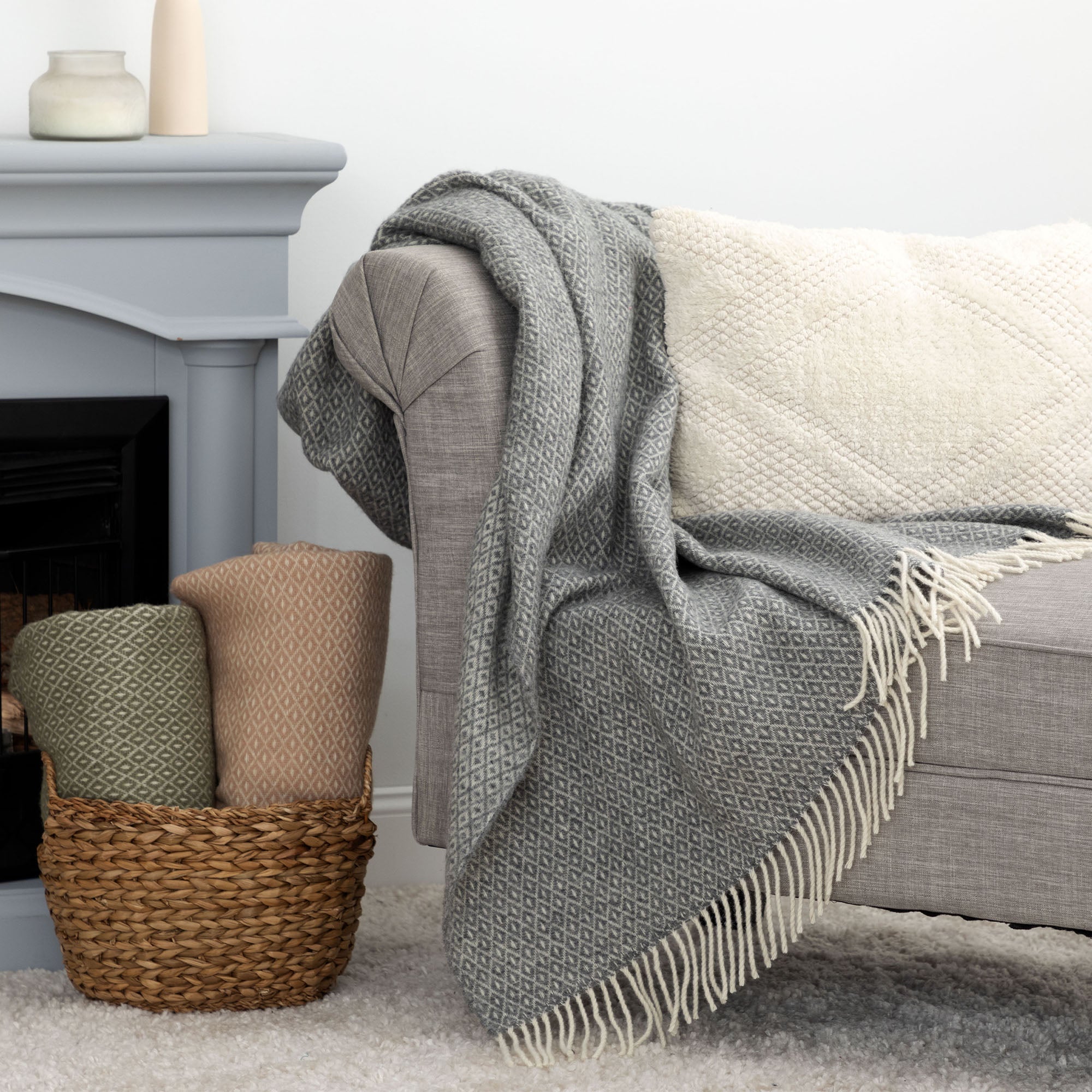 Cozy living room scene with a gray 100% wool throw blanket draped over a couch and more color options neatly rolled in a woven basket nearby.