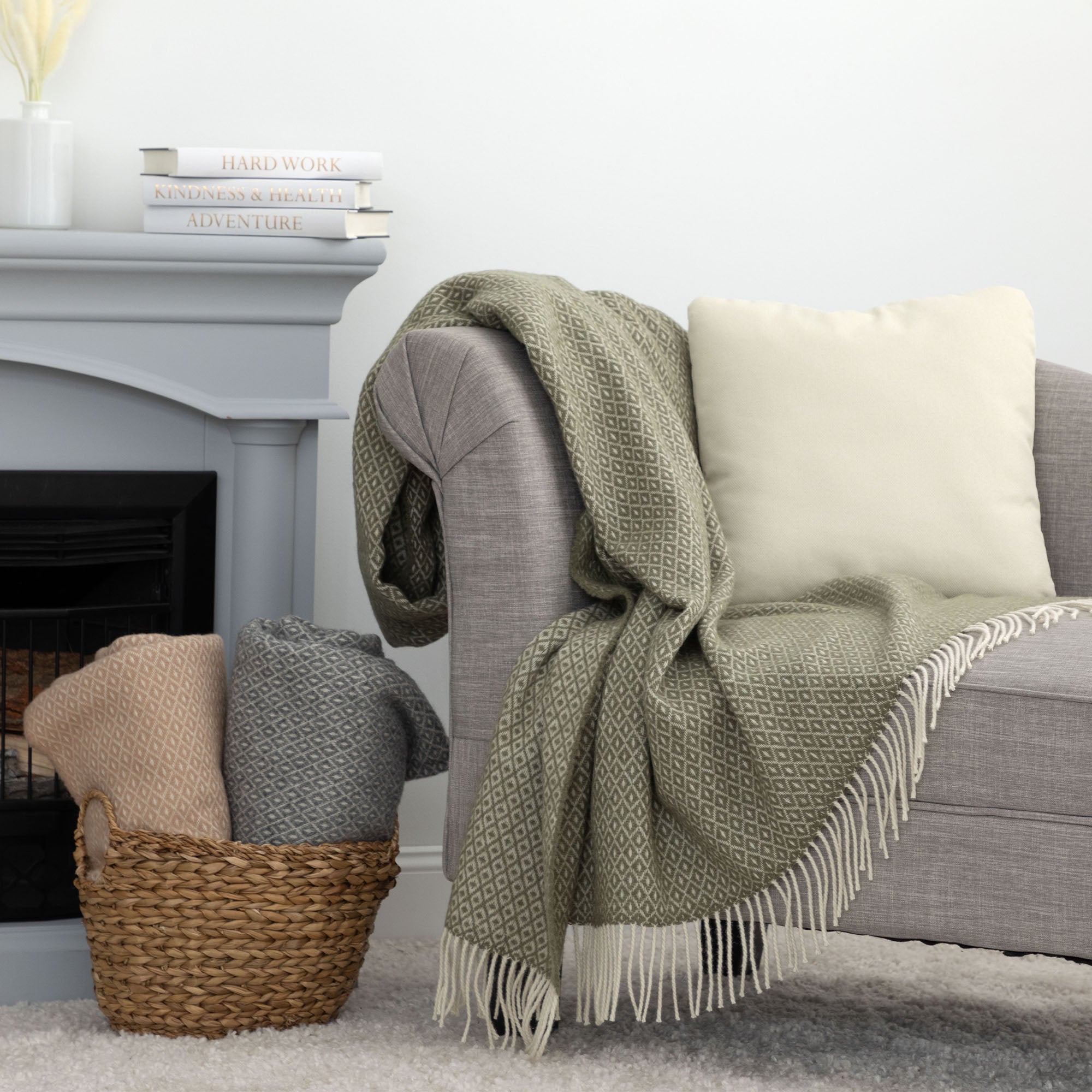 Draped olive green and cream diamond-patterned Ukrainian blanket with fringes, casually placed over a grey upholstered chair.