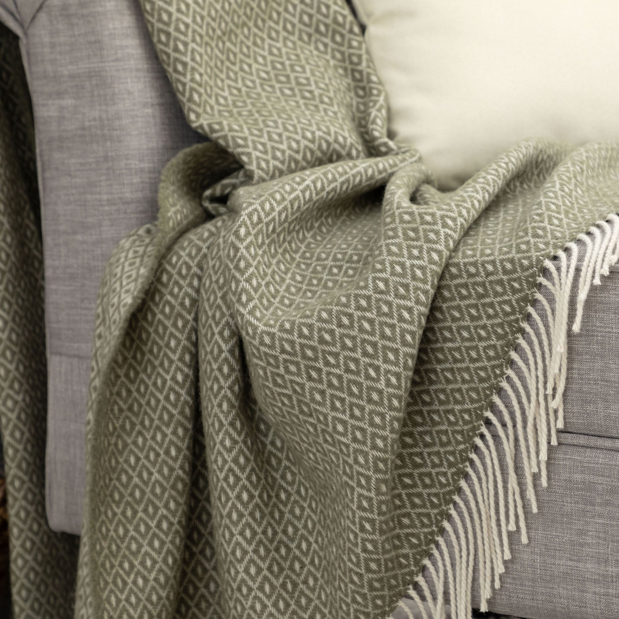 Close-up detail of the olive green and cream diamond-patterned Ukrainian blanket showing soft wool texture and fringes on a grey upholstered chair.