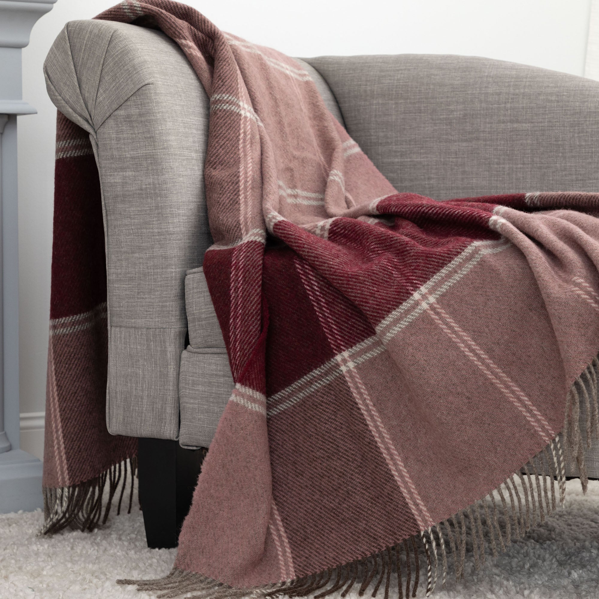 Warm plaid blanket in muted pinks and reds casually resting on a comfortable armchair.