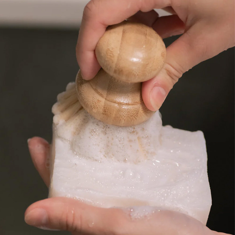 Hand using a wooden soap dispenser to apply soap to a bar of soap.