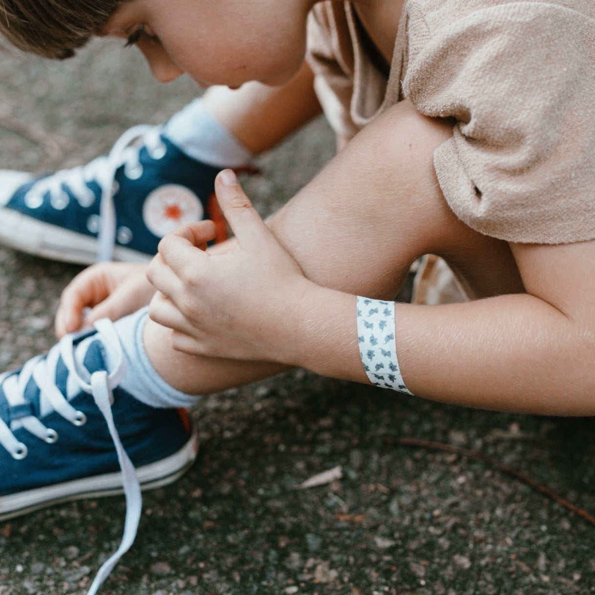Child kneeling in outdoor setting, with an animal-themed bandage strip covering a knee scrape.