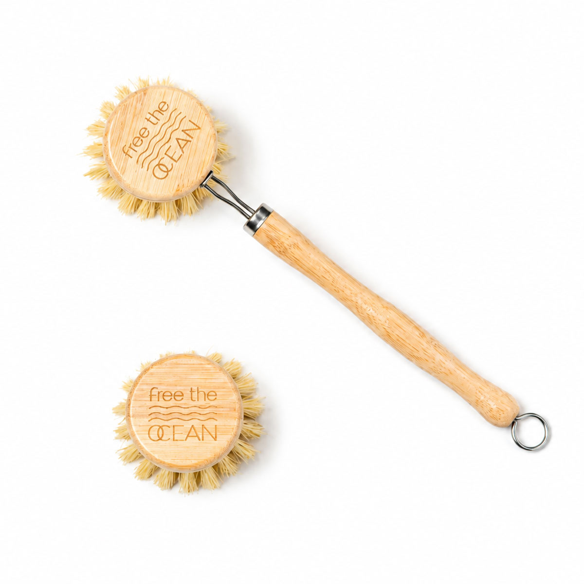 A bamboo-handled cleaning brush with natural bristles and a metal hanging loop, shown on a white background with one brush head viewed from above and another from the side. The brush head is engraved with the text 'free the OCEAN'.