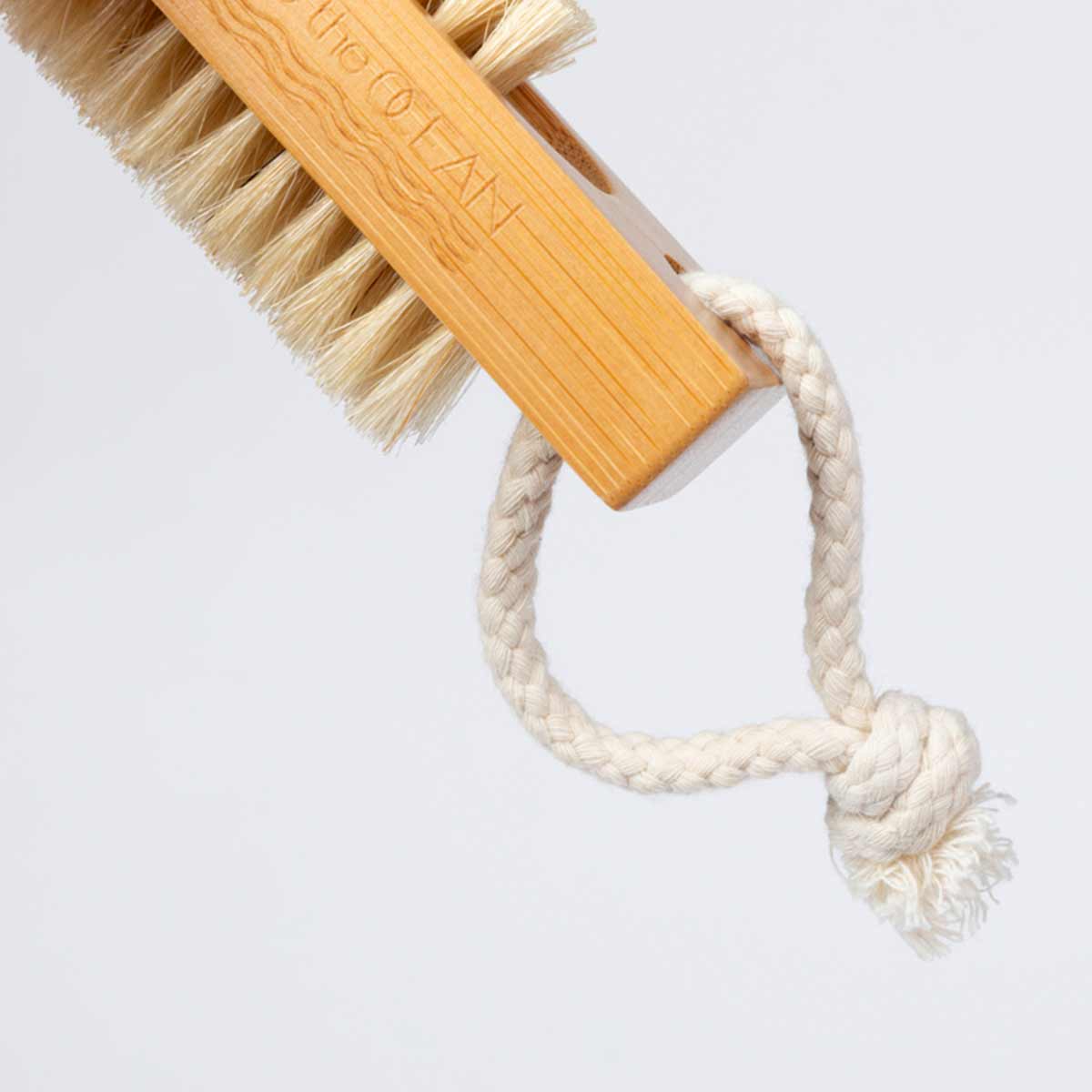 A close-up shot shows the handle of a bamboo nail brush with a braided rope loop attached to it. The Free the OCEAN logo is etched into the wood.
