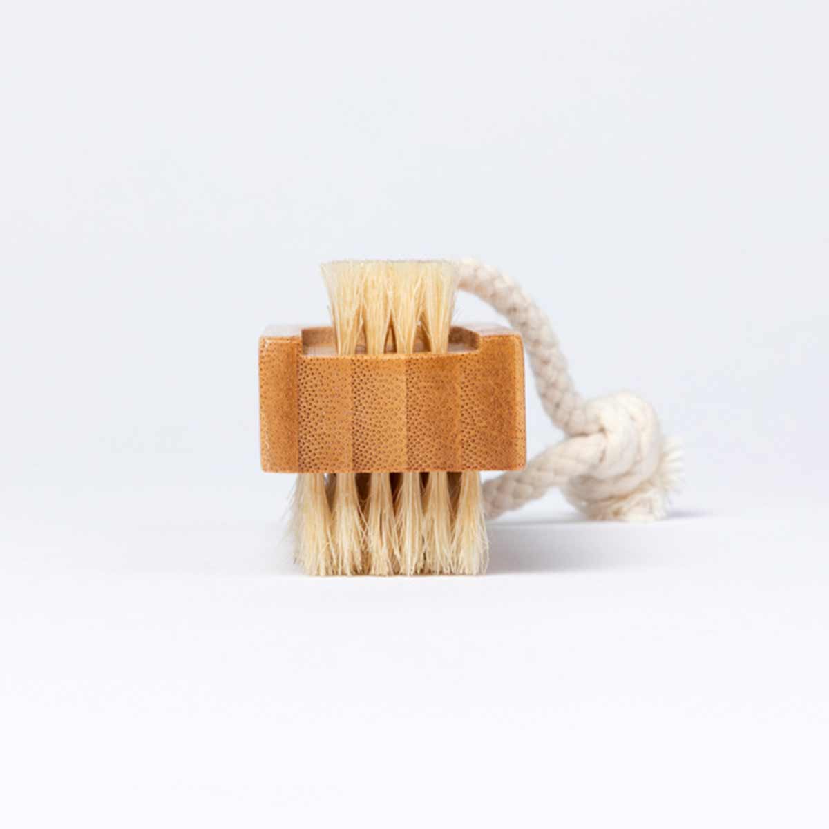 A bamboo nail brush with two sets of bristles is shown on its side. The brush has a braided rope loop attached to one end.
