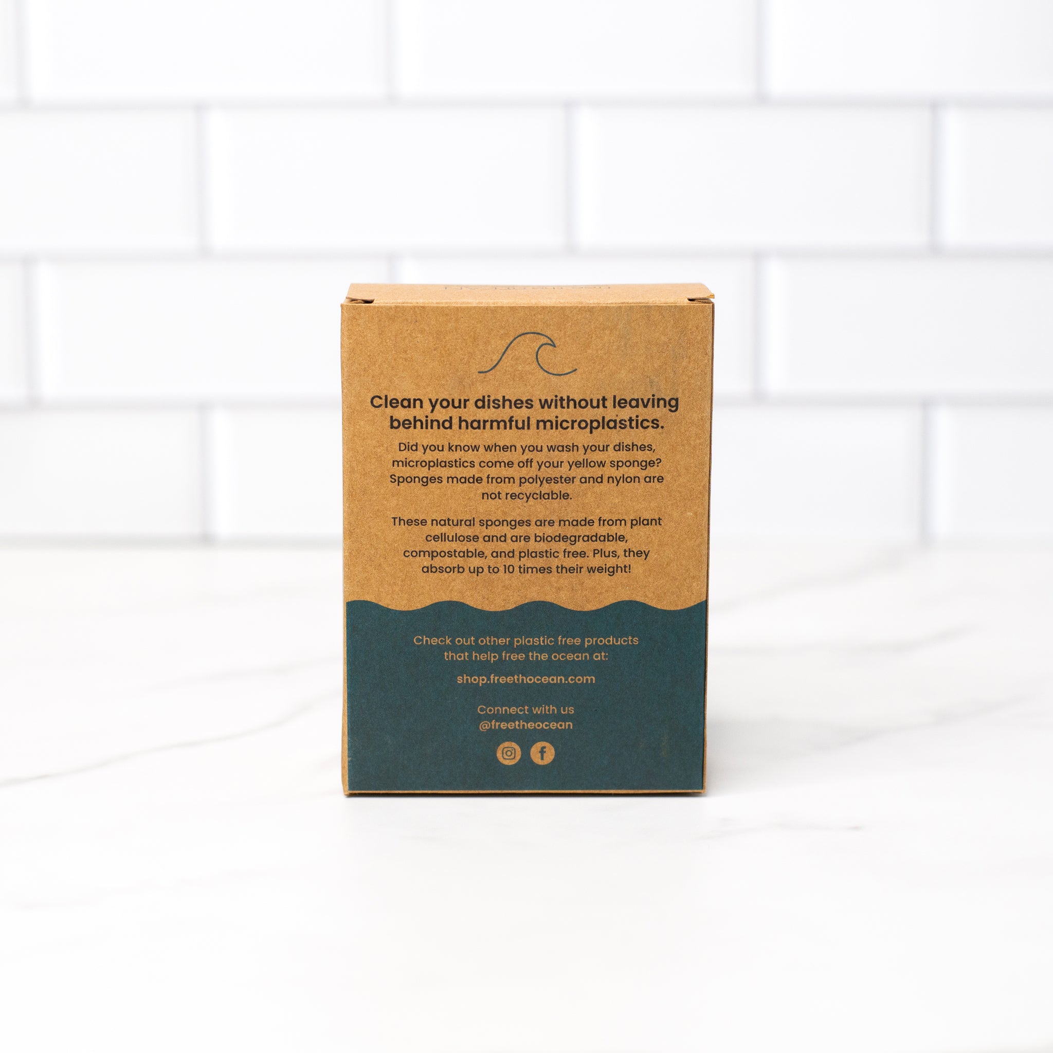 Back view of biodegradable kitchen sponges’ Kraft box packaging, featuring product care instructions and composting information, on a marble surface.