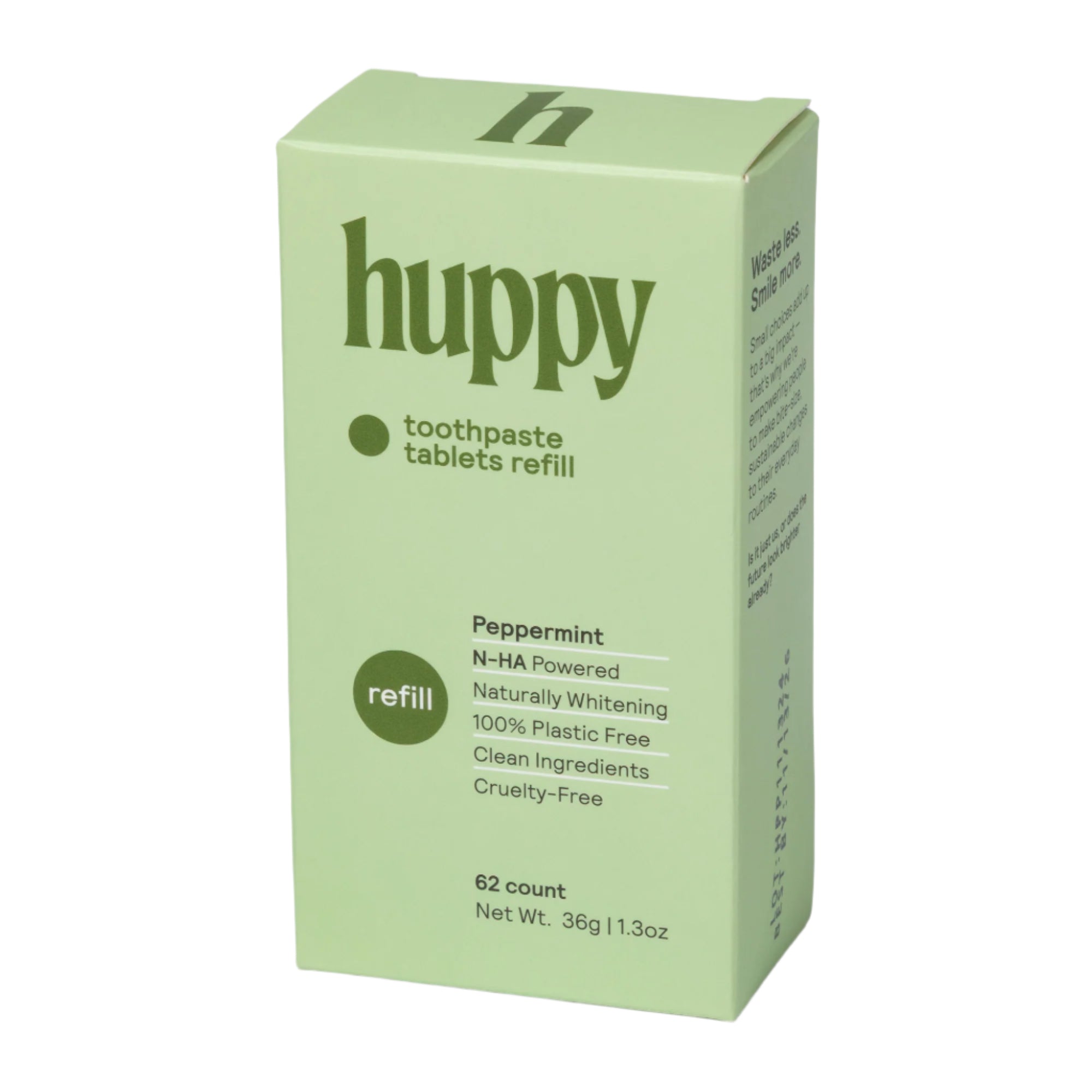 A green cardboard refill box of 'huppy' peppermint toothpaste tablets stands upright. The box highlights that the 62 tablets are "N-HA Powered," "100% Plastic Free," and "Cruelty-Free." The side of the box has a nice little message to "Waste less Smile more."