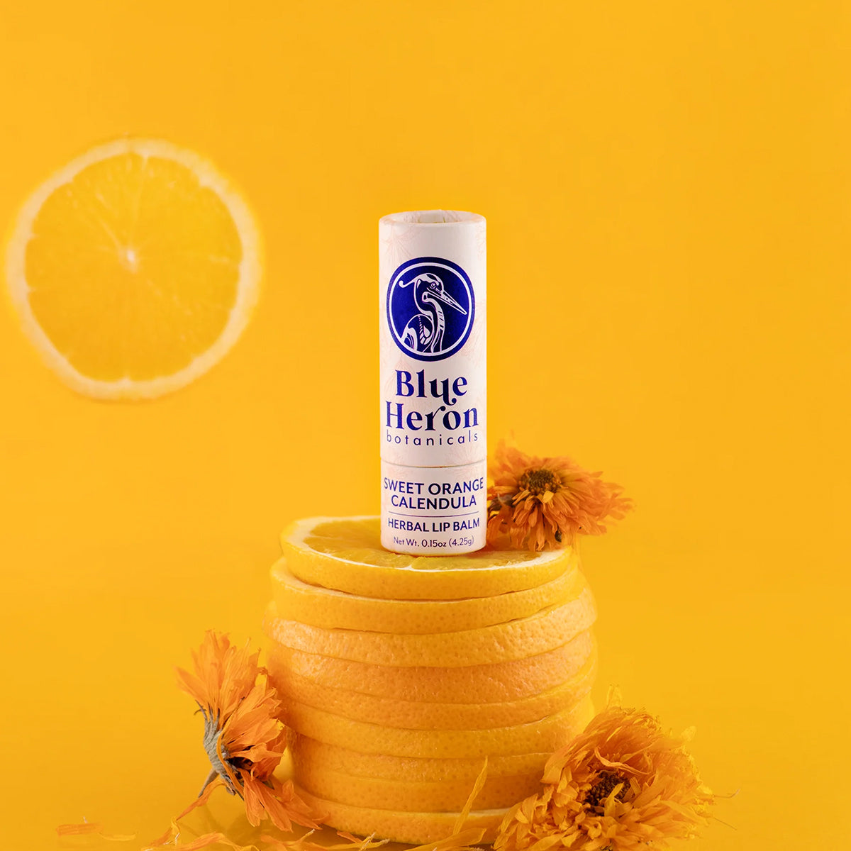 Blue Heron sweet orange calendula lip balm on a yellow background with orange slices and flowers