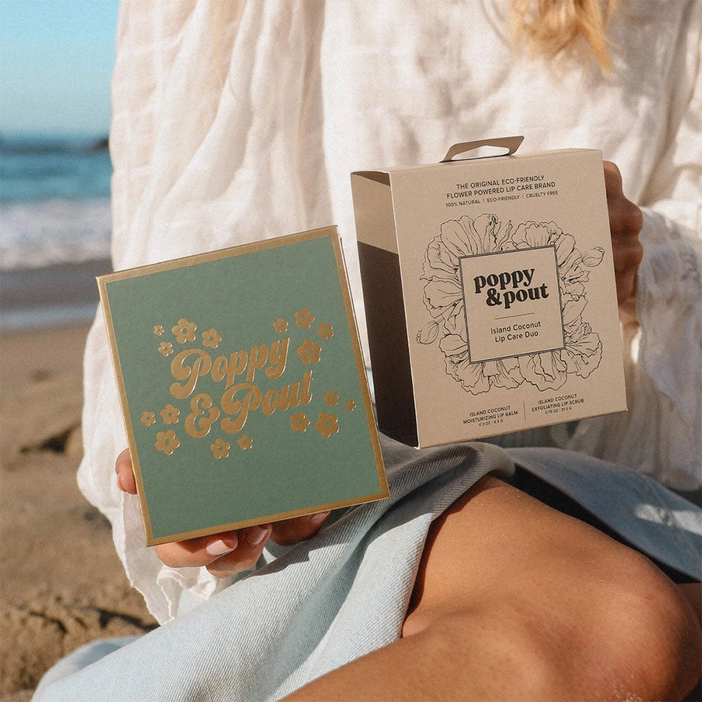 Person holding 'Poppy & Pout' lip care products on a beach