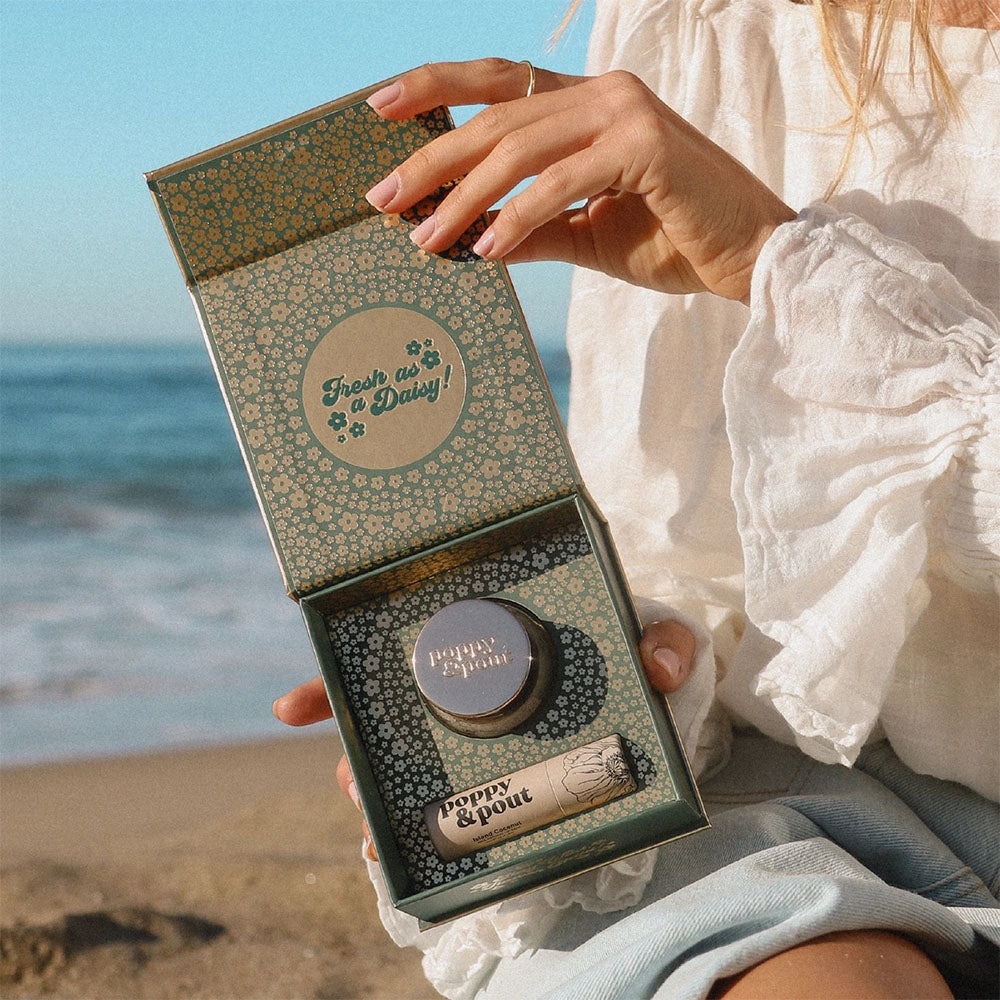 Hand holding a decorative Lip Care duo Island Coconut, with a beach in the background.