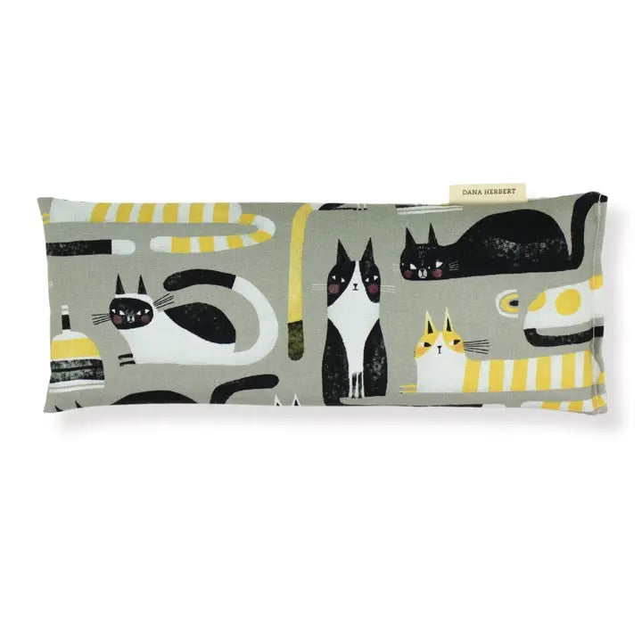 A rectangular eye pillow by Dana Herbert has a gray background with a pattern of black white and yellow cartoon cats on it.