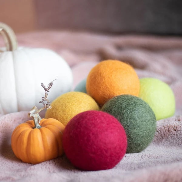 Harvest Collection wool dryer balls in warm fall tones resting on a burgundy towel next to a small pumpkin, eco-friendly, reduce drying time and static cling, made from 100% organic New Zealand wool